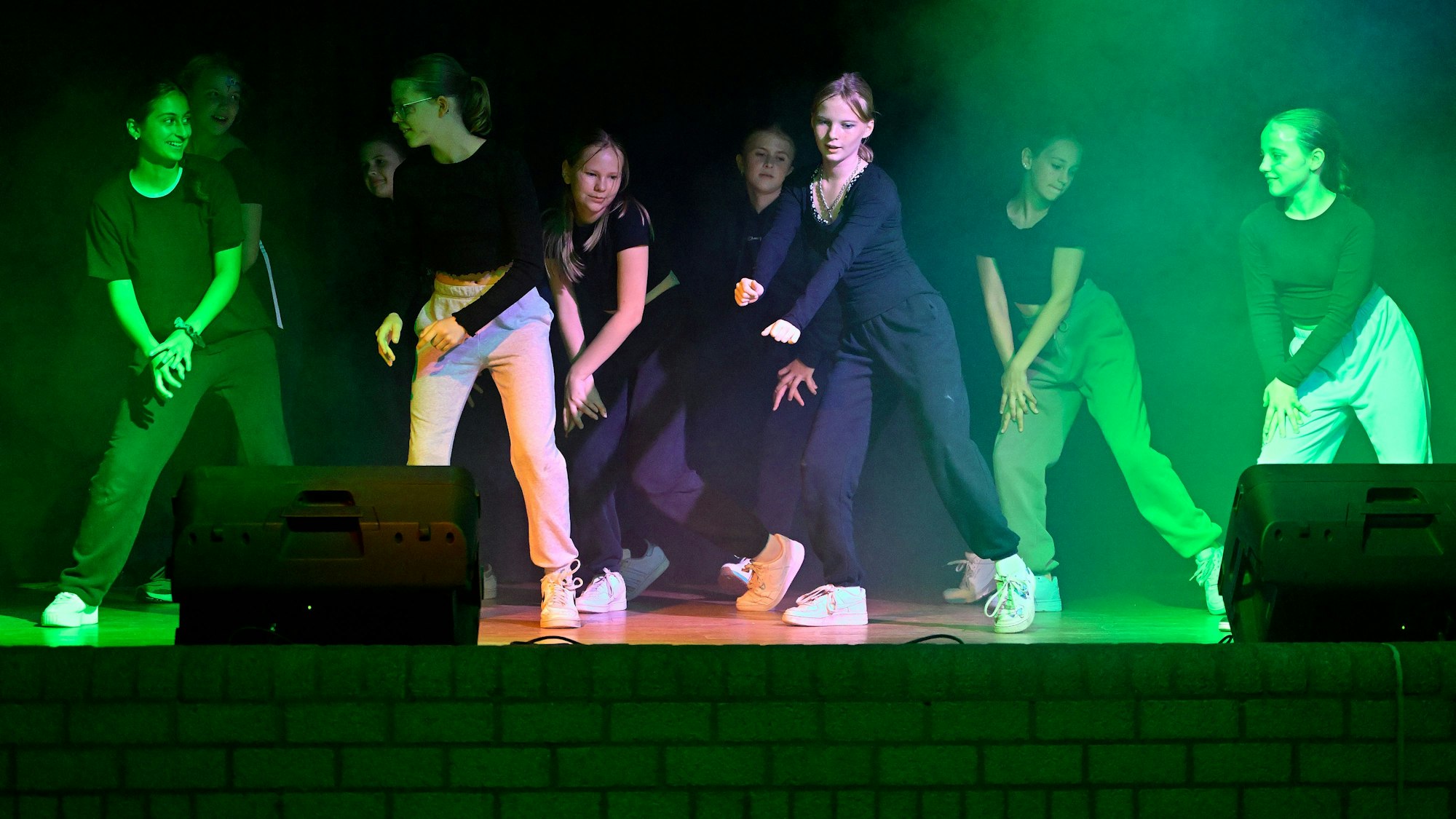 Jugendliche tanzen auf einer Bühne, die bunt angestrahlt ist.