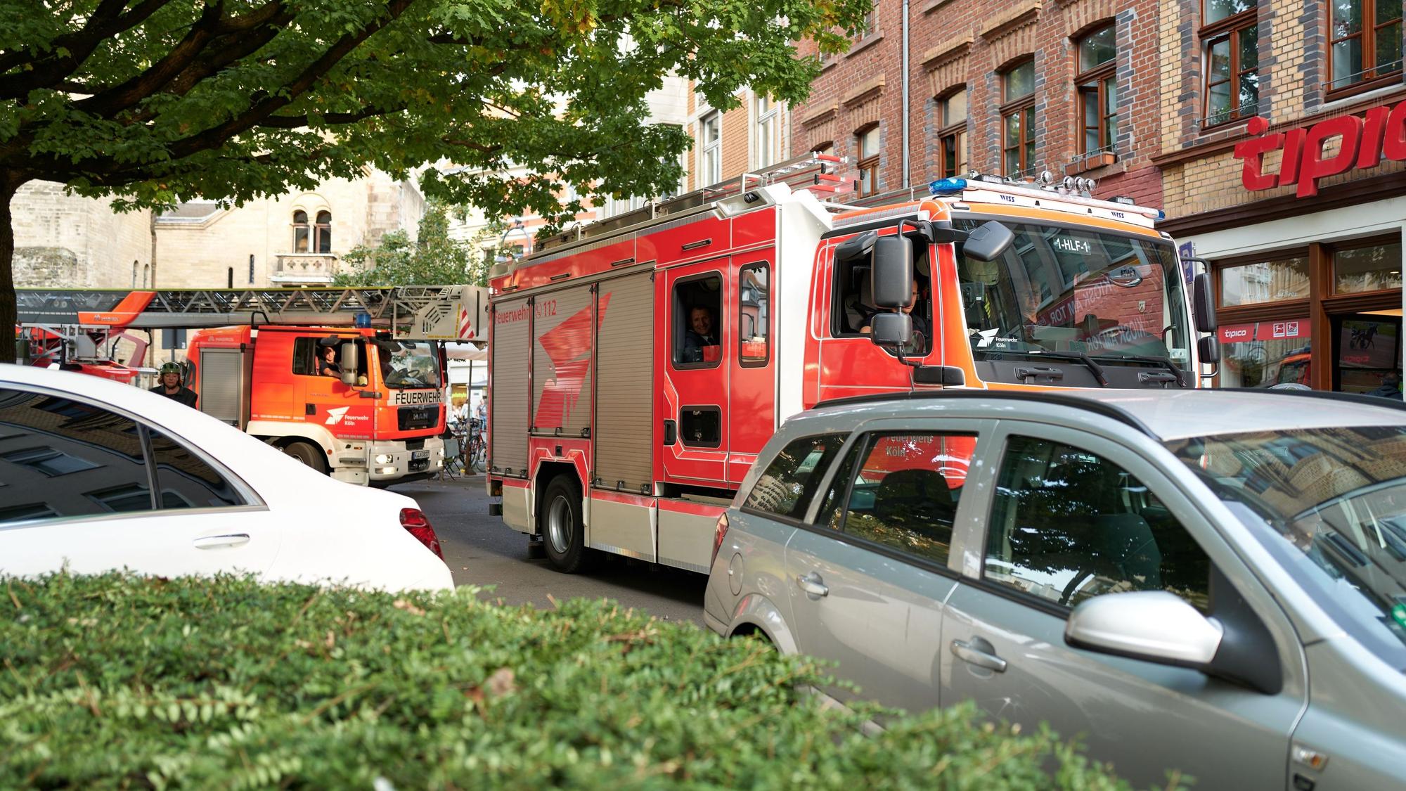 Zu sehen sind zwei Einsatzfahrzeuge der Kölner Feuerwehr, die an einem falsch parkenden Auto vorbeifahren wollen.