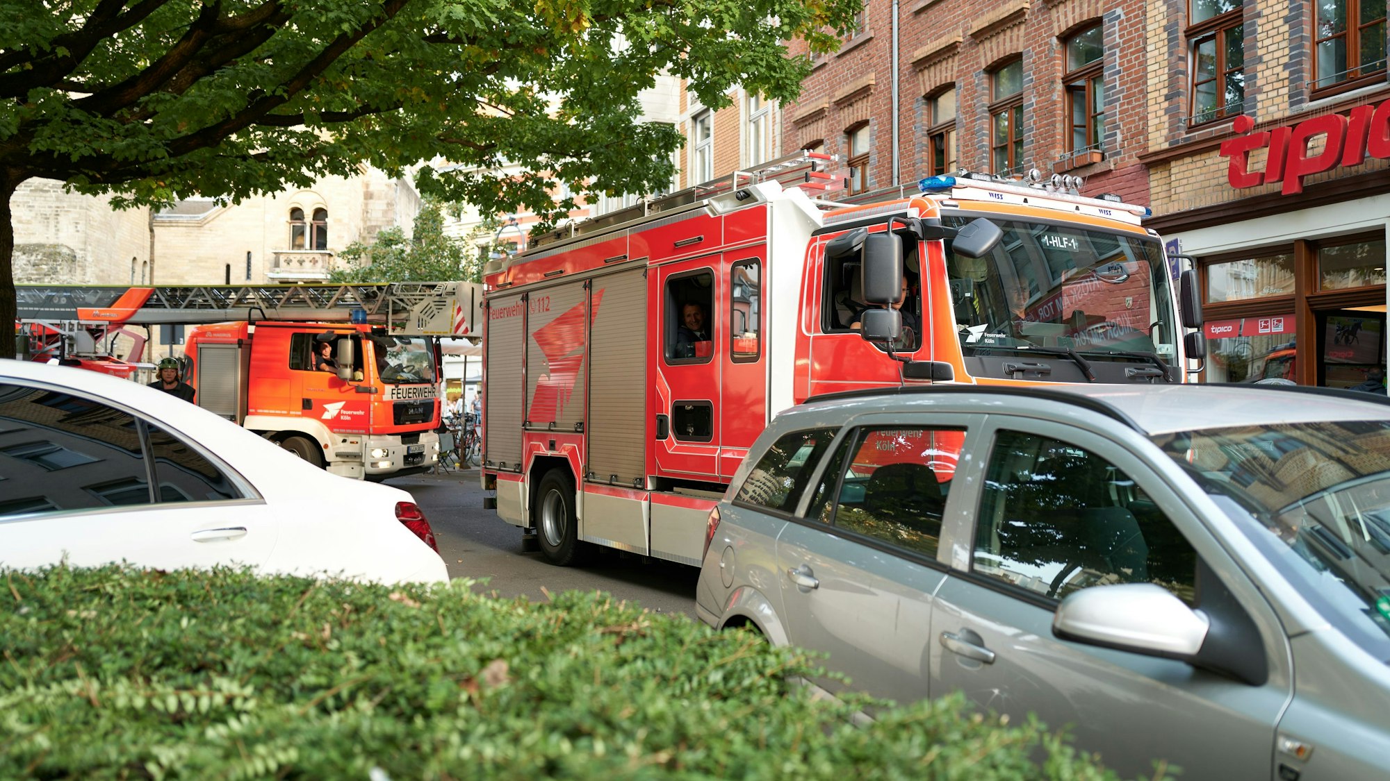 Zu sehen sind zwei Einsatzfahrzeuge der Kölner Feuerwehr, die an einem falsch parkenden Auto vorbeifahren wollen.