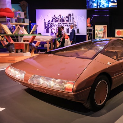 Das Konzeptfahrzeug "Citroen Karin" aus dem Jahr 1980 steht in der Bundeskunsthalle. Es ist rötlich und geometrisch-schnittig. Im Hintergrund weitere bunte Kunstwerke und Besucher.