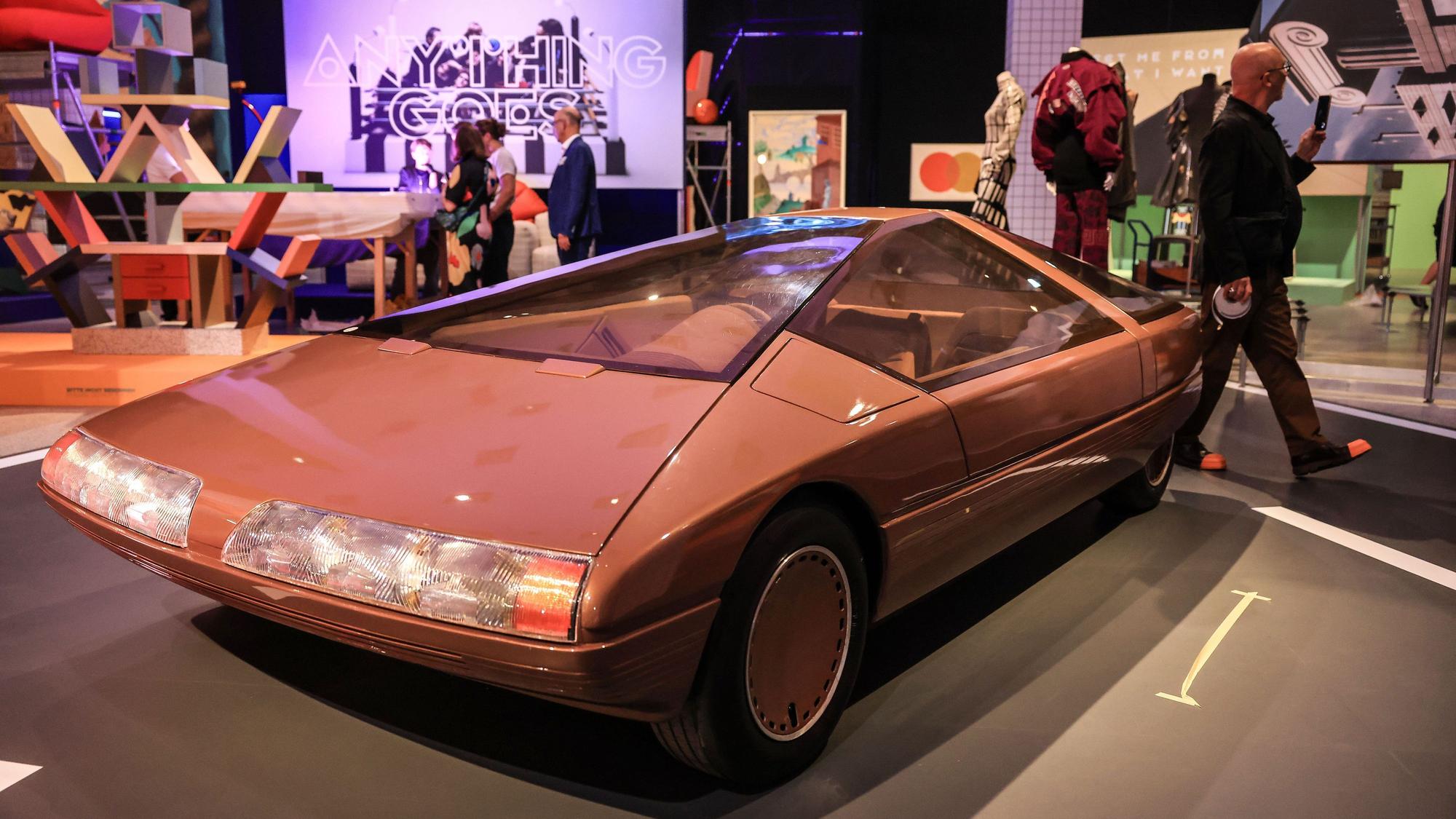 Das Konzeptfahrzeug "Citroen Karin" aus dem Jahr 1980 steht in der Bundeskunsthalle. Es ist rötlich und geometrisch-schnittig. Im Hintergrund weitere bunte Kunstwerke und Besucher.