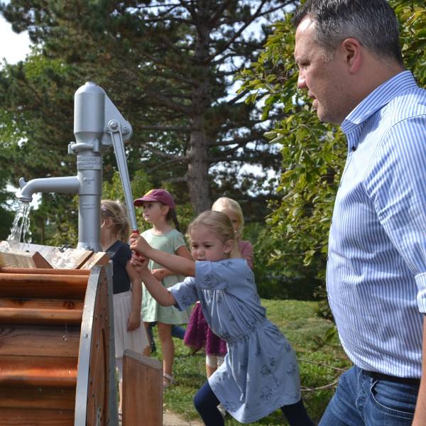 Euskirchens Bürgermeister Sacha Reichelt (r.) und Stiftungsgeschäftsführer Christoph Palm (l.) schauen zu, wie die Kinder der Kita Großbüllesheim die Wassermatschanlage bedienen. Aus einer Pumpe läuft Wasser.