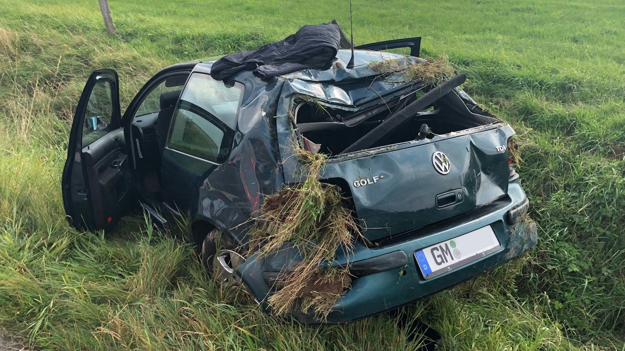 Der deformierte VW Golf liegt in der Wiese.
