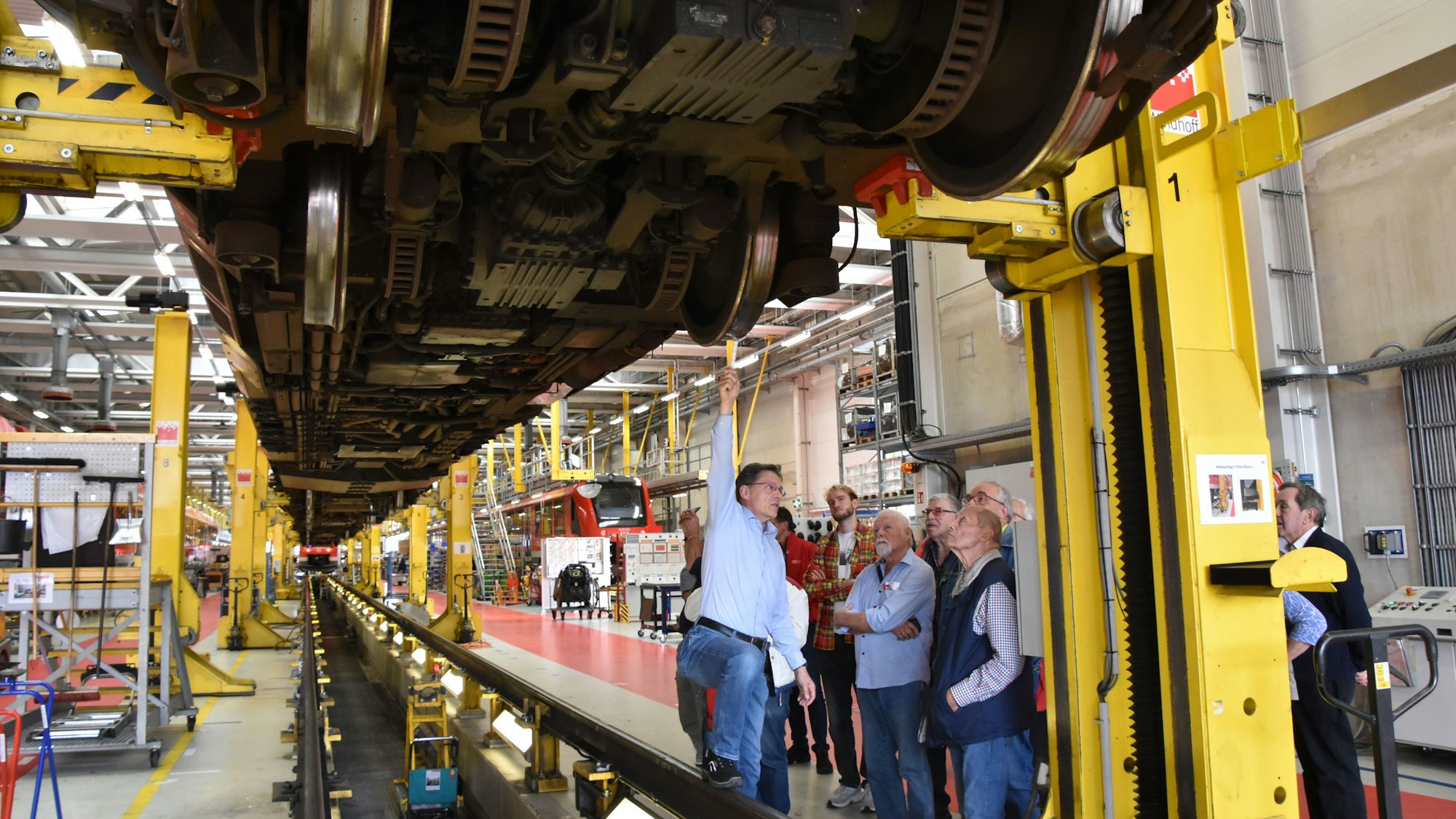 Ein Mann im blauen Hemd zeigt von unten auf Komponenten eines auf 2,5 Meter aufgebockten Zuges.
