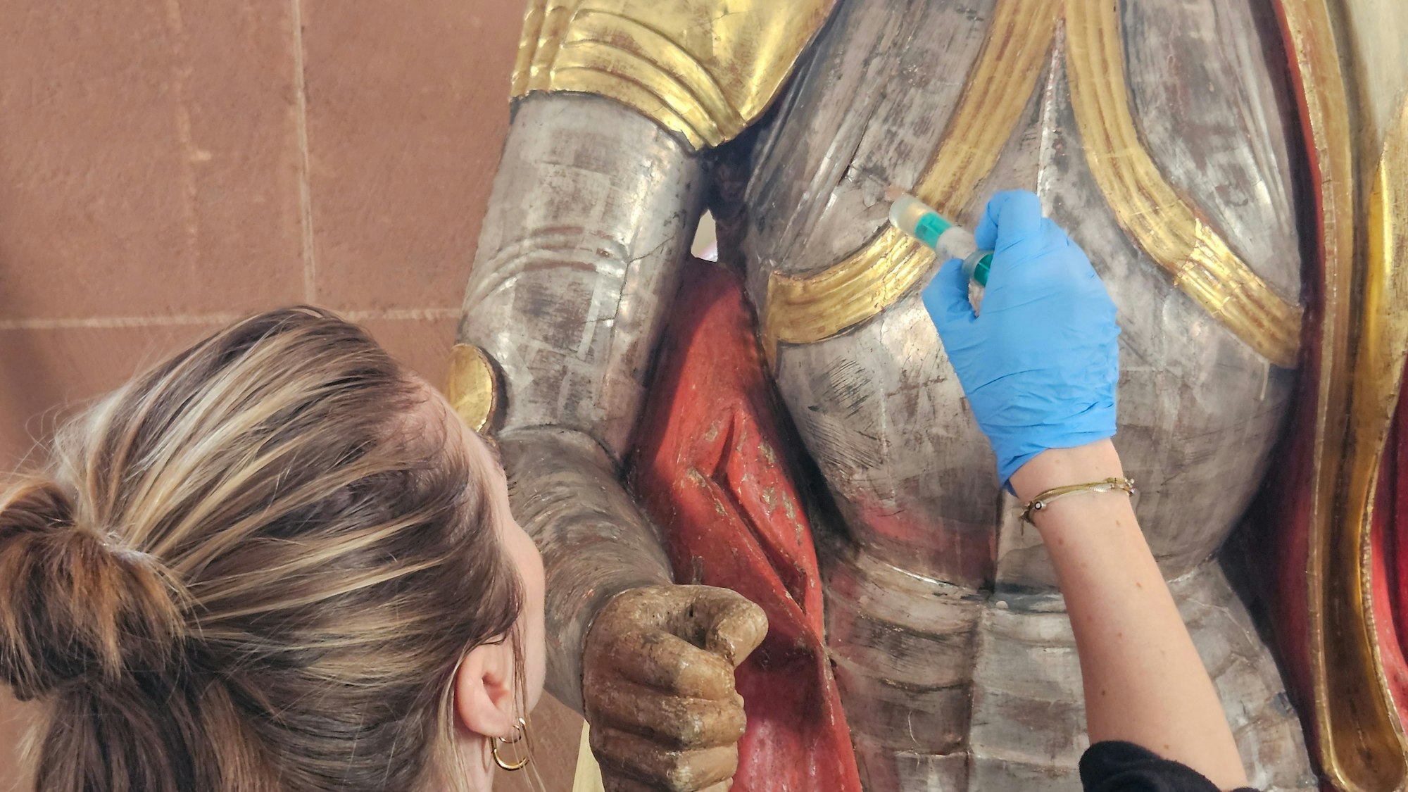 Eine Frau spritzt mit einer Spitze Harz unter eine abstehende Stelle an einer Figur.