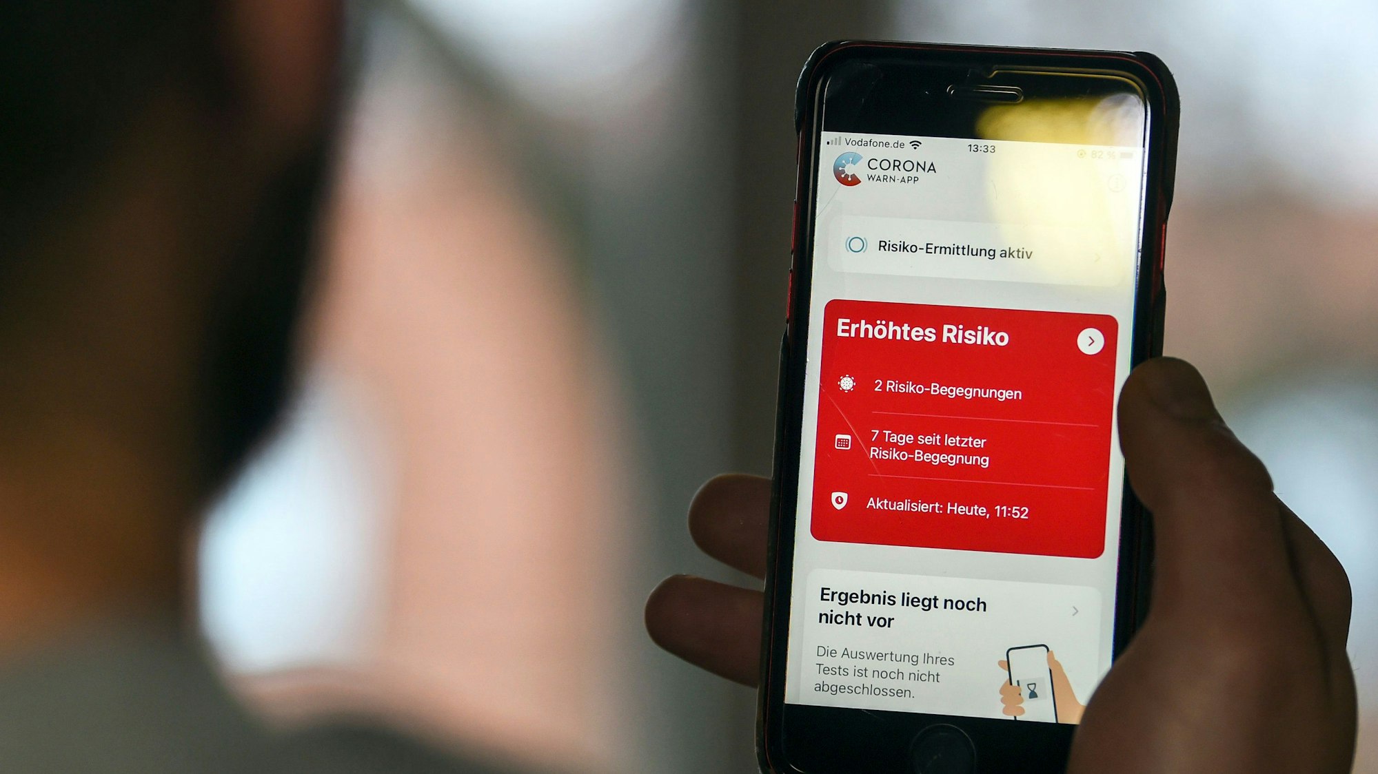 Ein Mann hält ein Smartphone in der Hand, auf dem die Corona-App in einem roten Feld „Erhöhtes Risiko“ anzeigt.