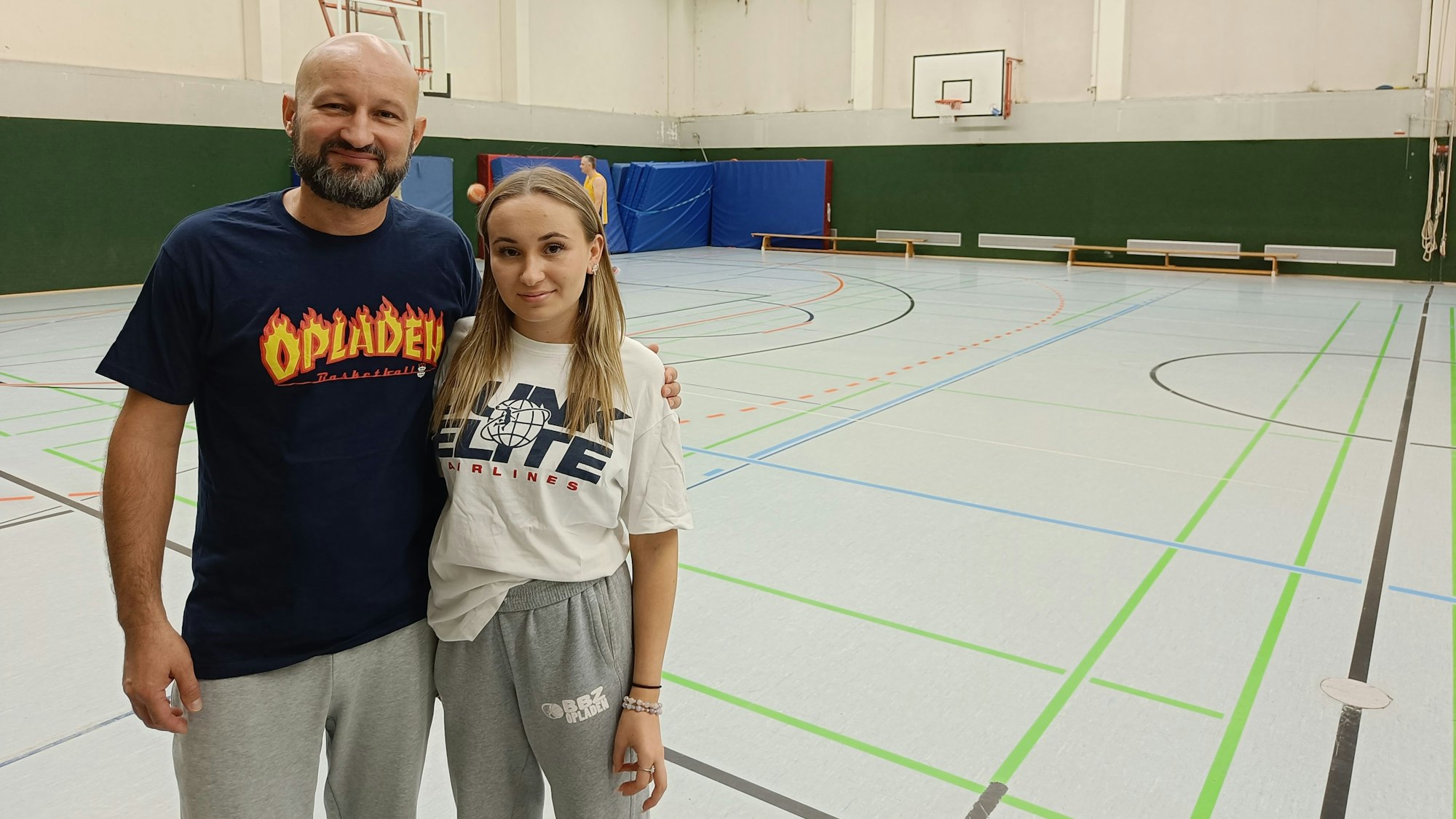 Ein Mann und eine junge Frau stehen vor einem Basketball-Feld.