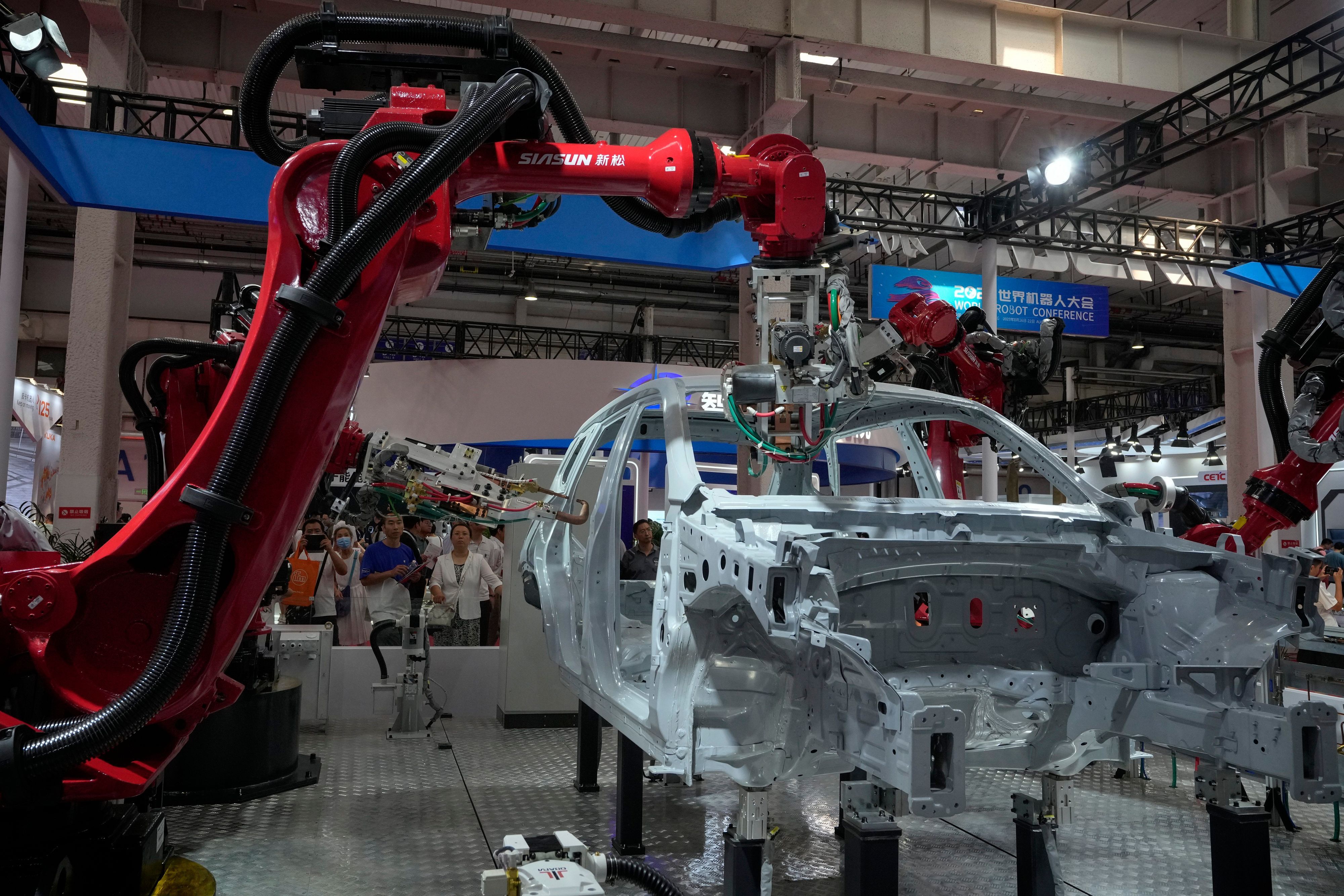 Besucher betrachten die Roboterarme, die während der jährlichen Weltroboterkonferenz im Etrong International Exhibition and Convention Center am 17. August 2023 am Stadtrand von Peking einen Fahrzeugrahmen zusammenbauen.