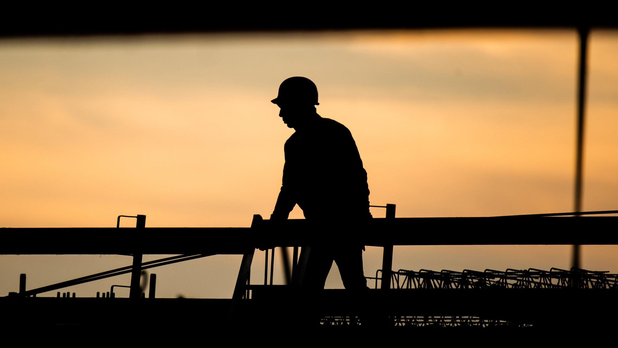 ARCHIV - 31.08.2021, Niedersachsen, Hannover: Die Silhouette eines Bauarbeiters zeichnet sich auf einer Baustelle vor dem verfärbten Morgenhimmel ab. Die schlechte Konjunkturentwicklung in Deutschland sorgt einer Studie zufolge für einen leichten Rückgang des Fachkräftemangels.