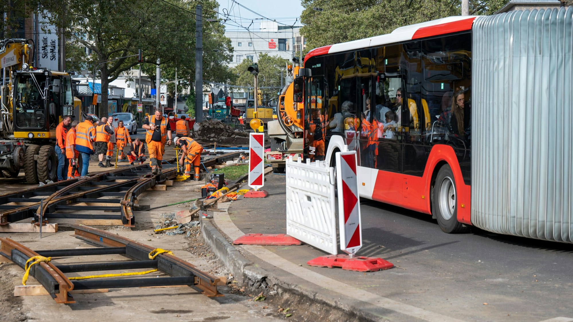 Bauarbeiter arbeiten am Gleisbett am Neumarkt, neben ihnen fährt ein Bus vorbei.