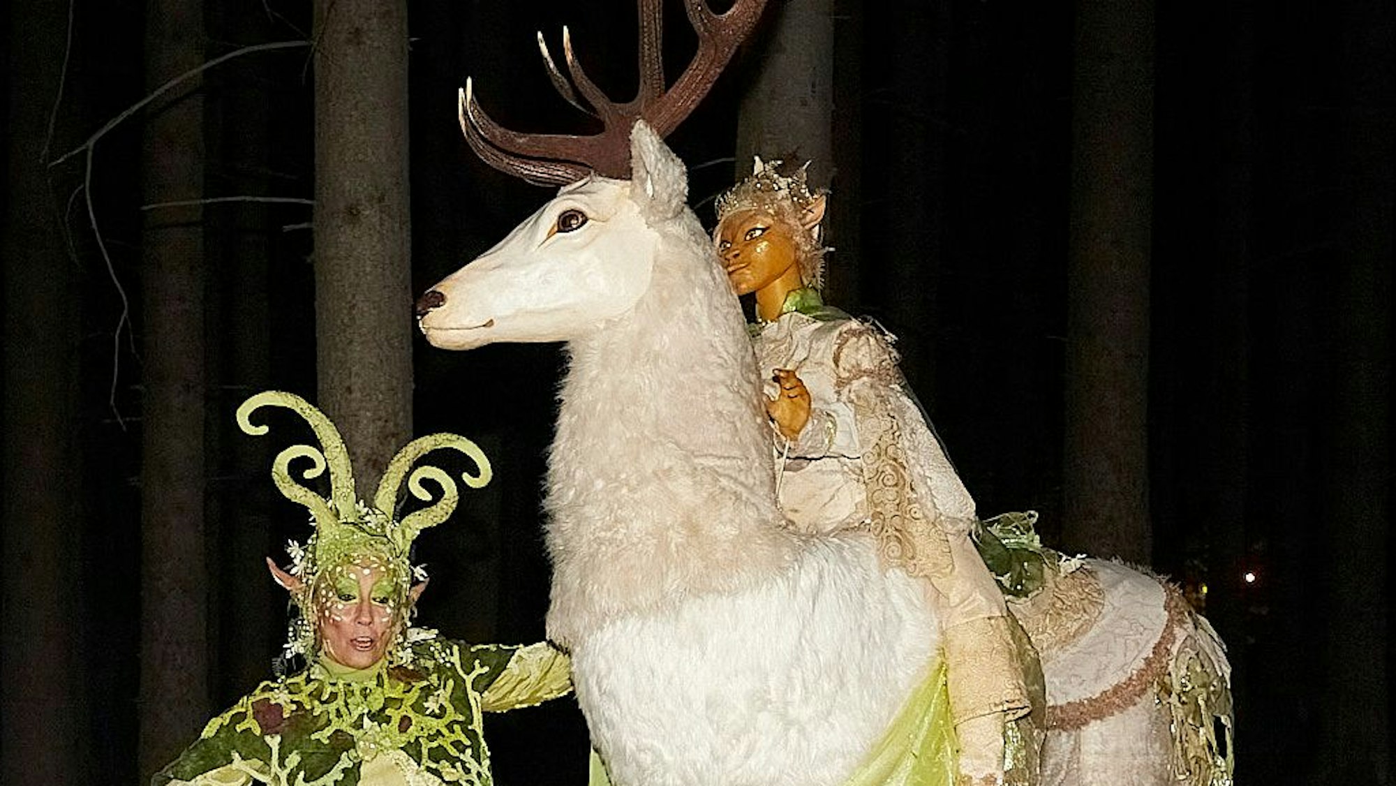 Eine fantasievoll verkleidete Frau präsentiert während der Hubertusnacht einen weißen Hirsch aus Stoff. Auf seinem Rücken sitzt eine Mädchenfigur.