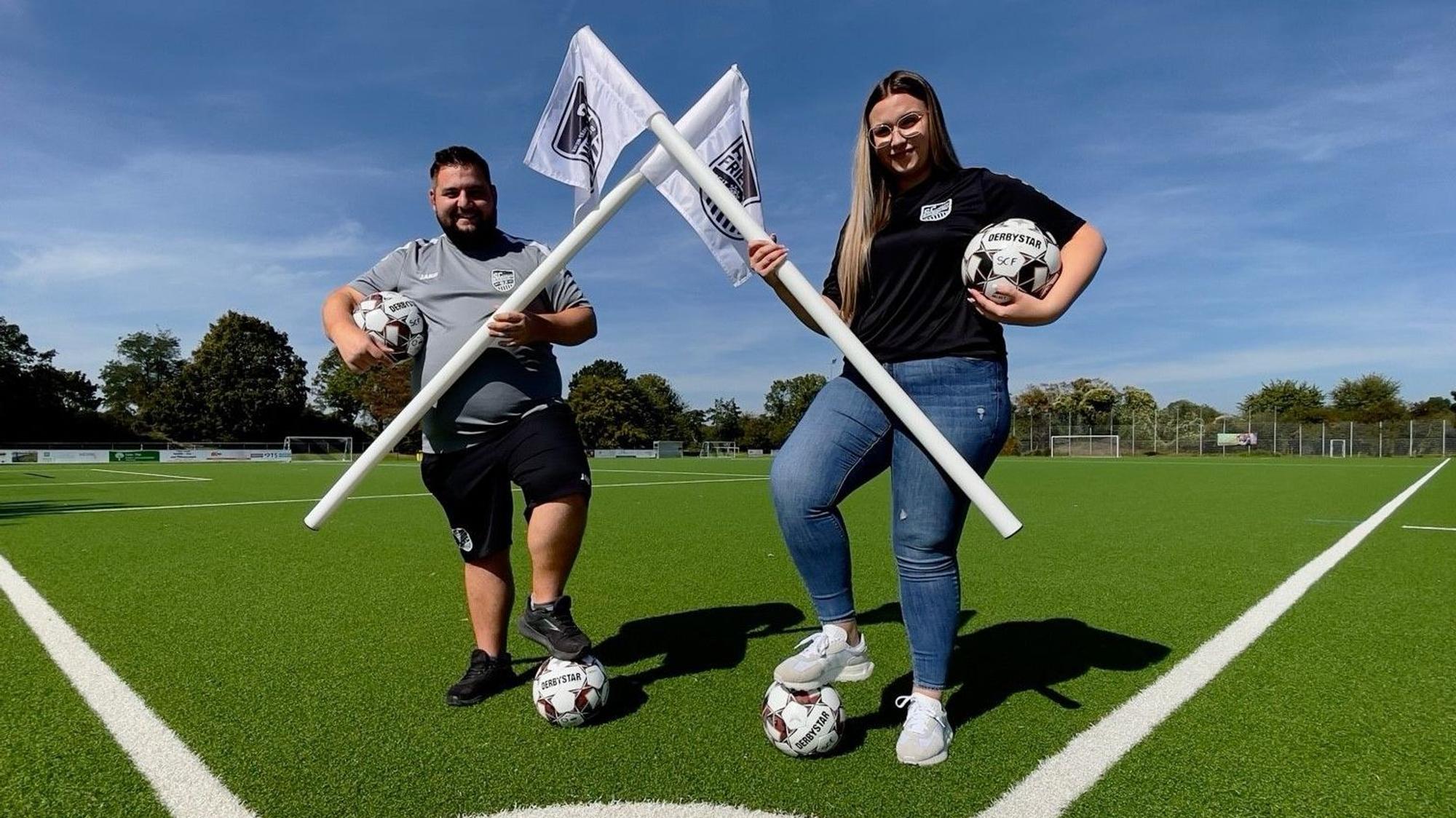 Die Inklusionsbeauftragte Luisa Büdding steht mit dem SC-Vorsitzenden Yannick Braun auf einem Fußballplatz.