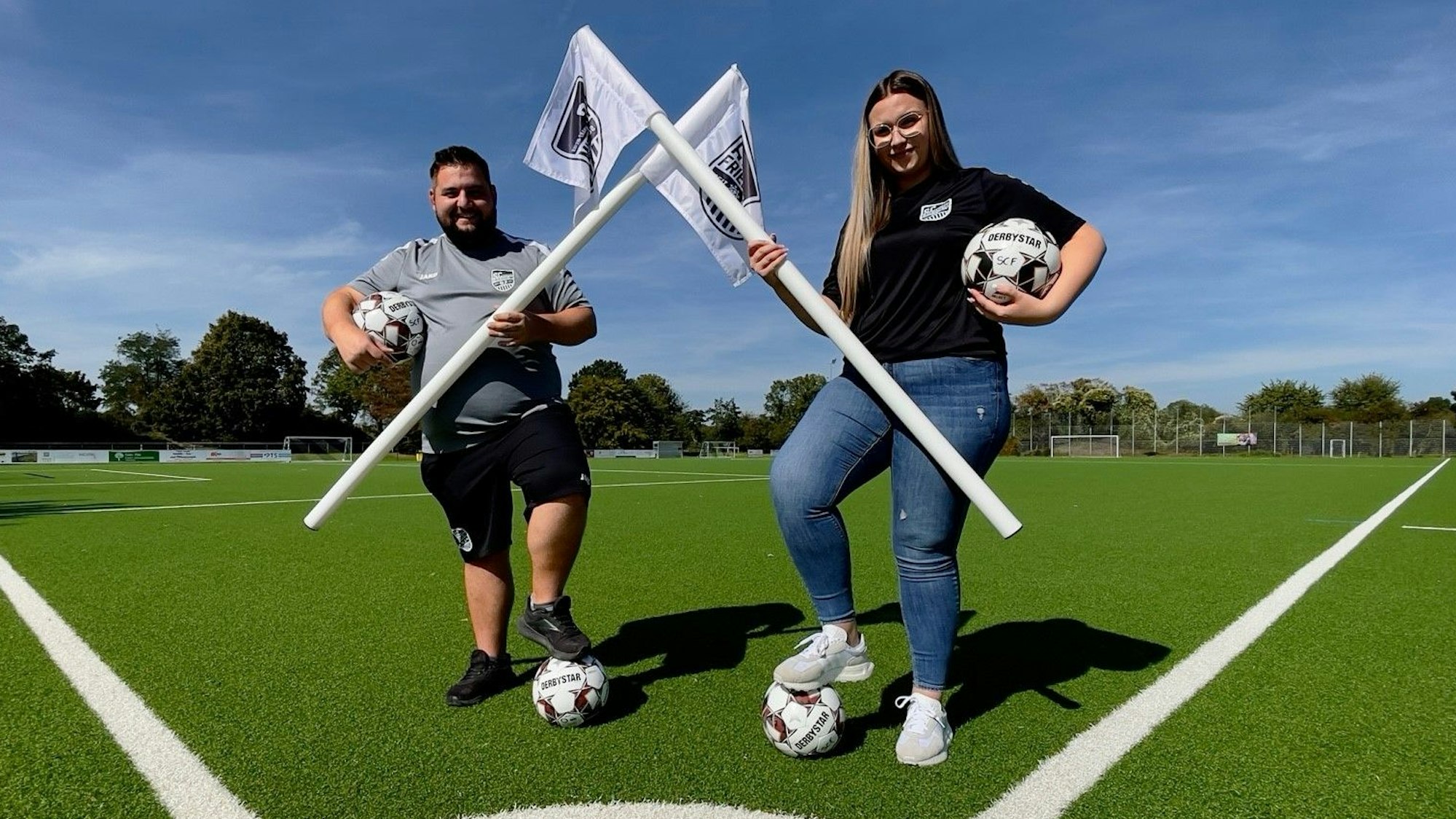 Die Inklusionsbeauftragte Luisa Büdding steht mit dem SC-Vorsitzenden Yannick Braun auf einem Fußballplatz.