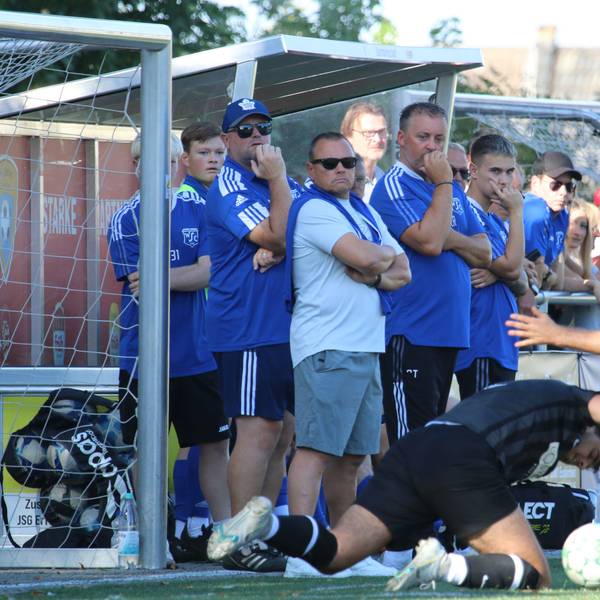 Ein Zweikampf, wobi ein Spieler auf dem Boden fällt, wird von der Auswechselbank verfolgt.
