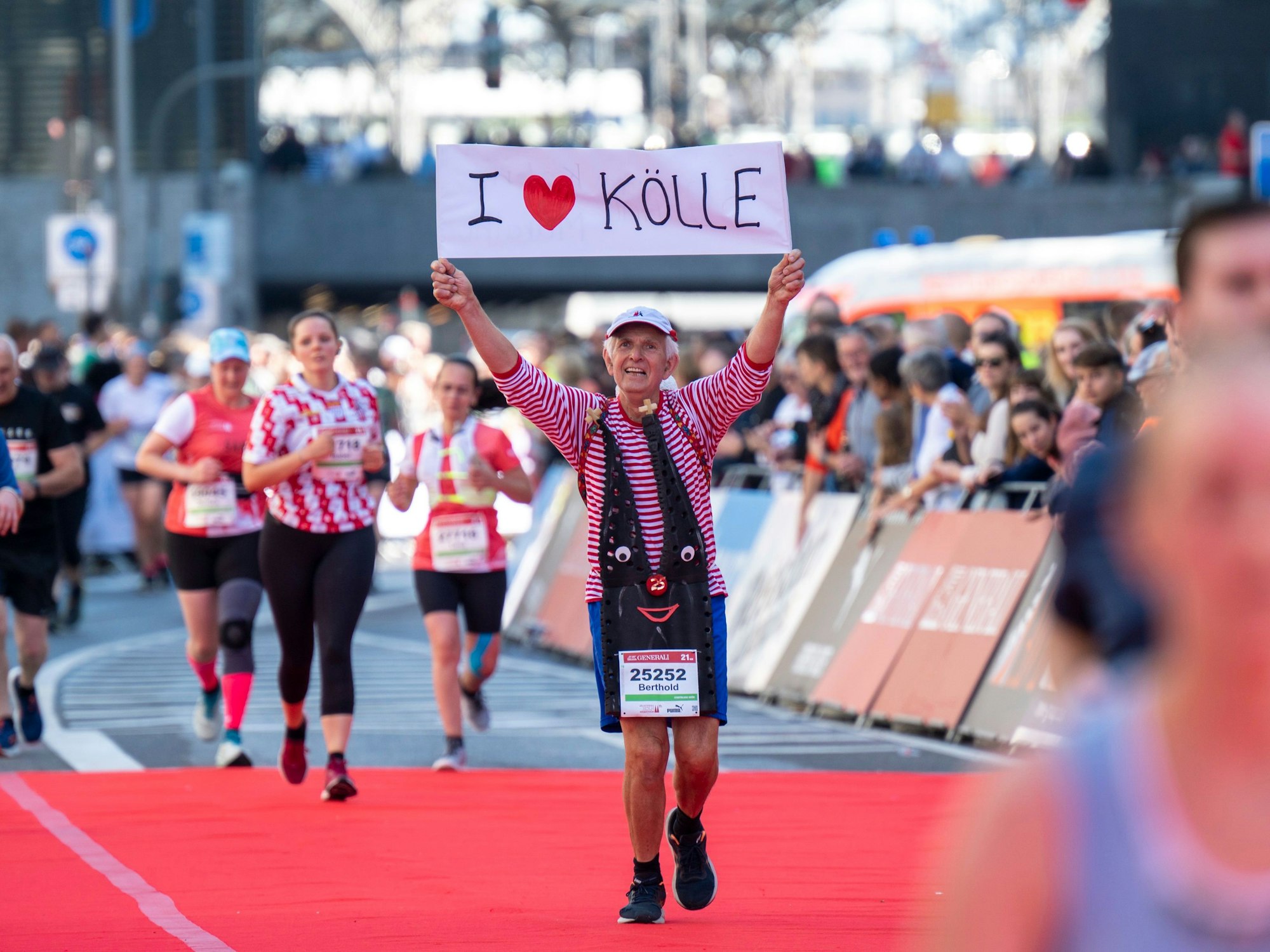 Beim 25. Köln-Marathon hält Stamm-Läufer Berthold Mausbach ein Schild in die Höhe.