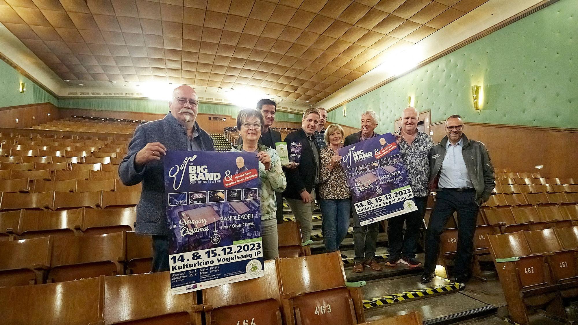 Im Kulturkino in Vogelsang machen Organisatoren und Akteure Werbung für das Weihnachtsprogramm der Bundeswehr-Bigband. Einige halten Plakate in den Händen.