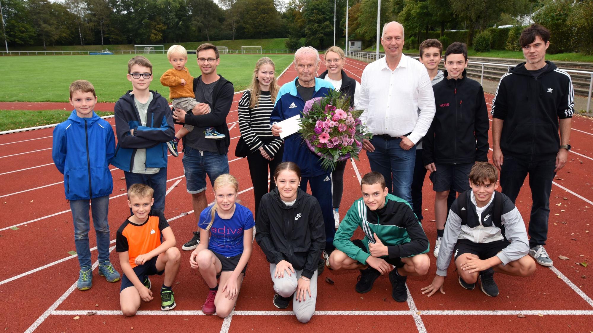 Kinder und weitere Sportler auf einer Laufbahn mit Oswald Pankalla, der einen Blumenstrauß in der Hand hält.
