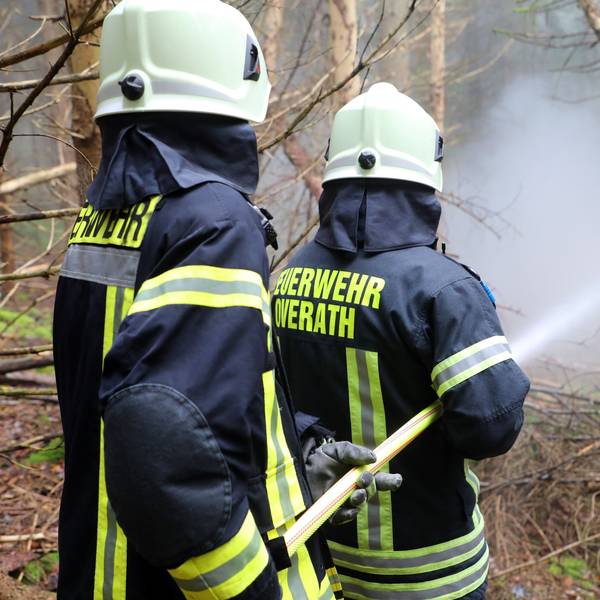 Zwei Feuerwehrleute der Feuerwehr Overath halten einen C-Schlauch auf Übungsrauch in einem Fichtenwald.