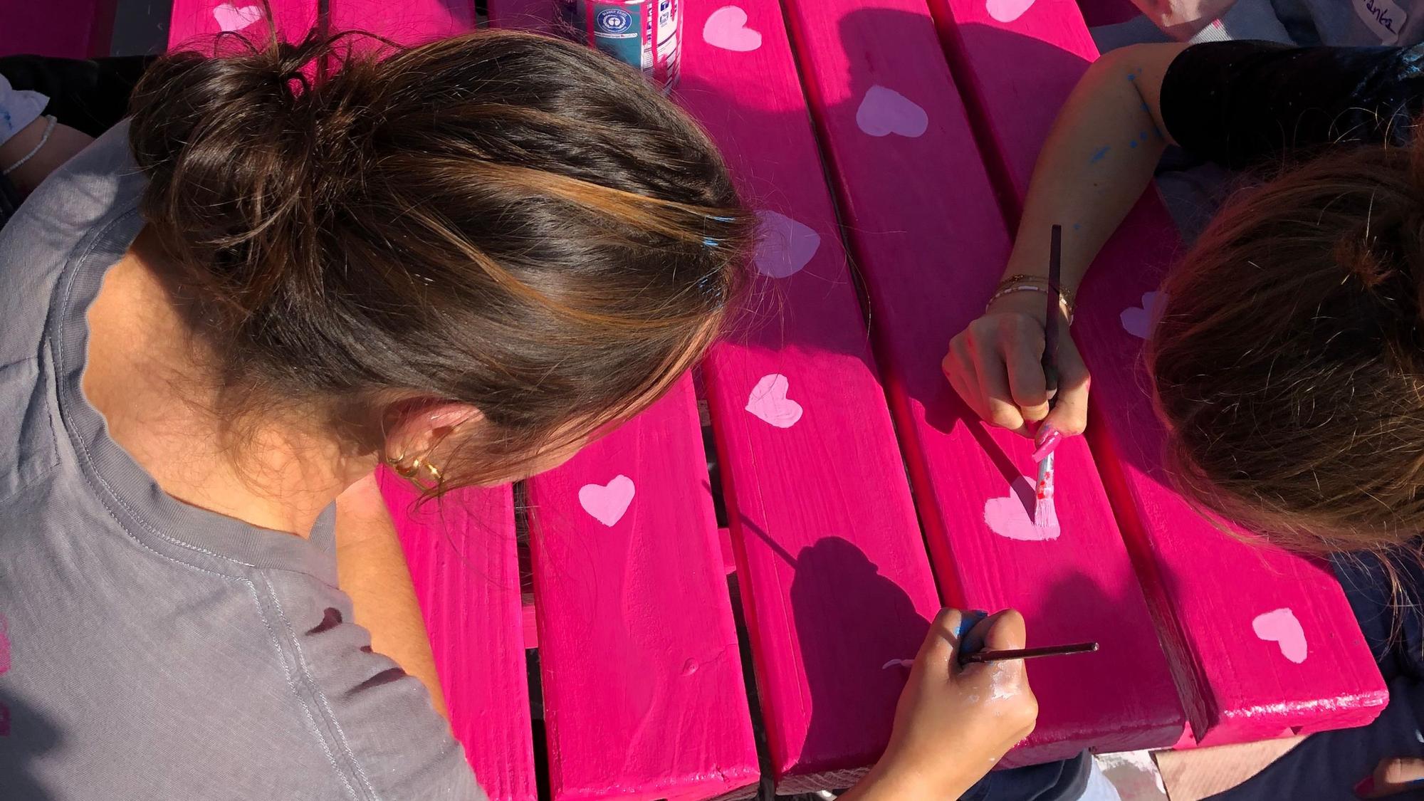 Schüler malen auf eine pinke Bank.