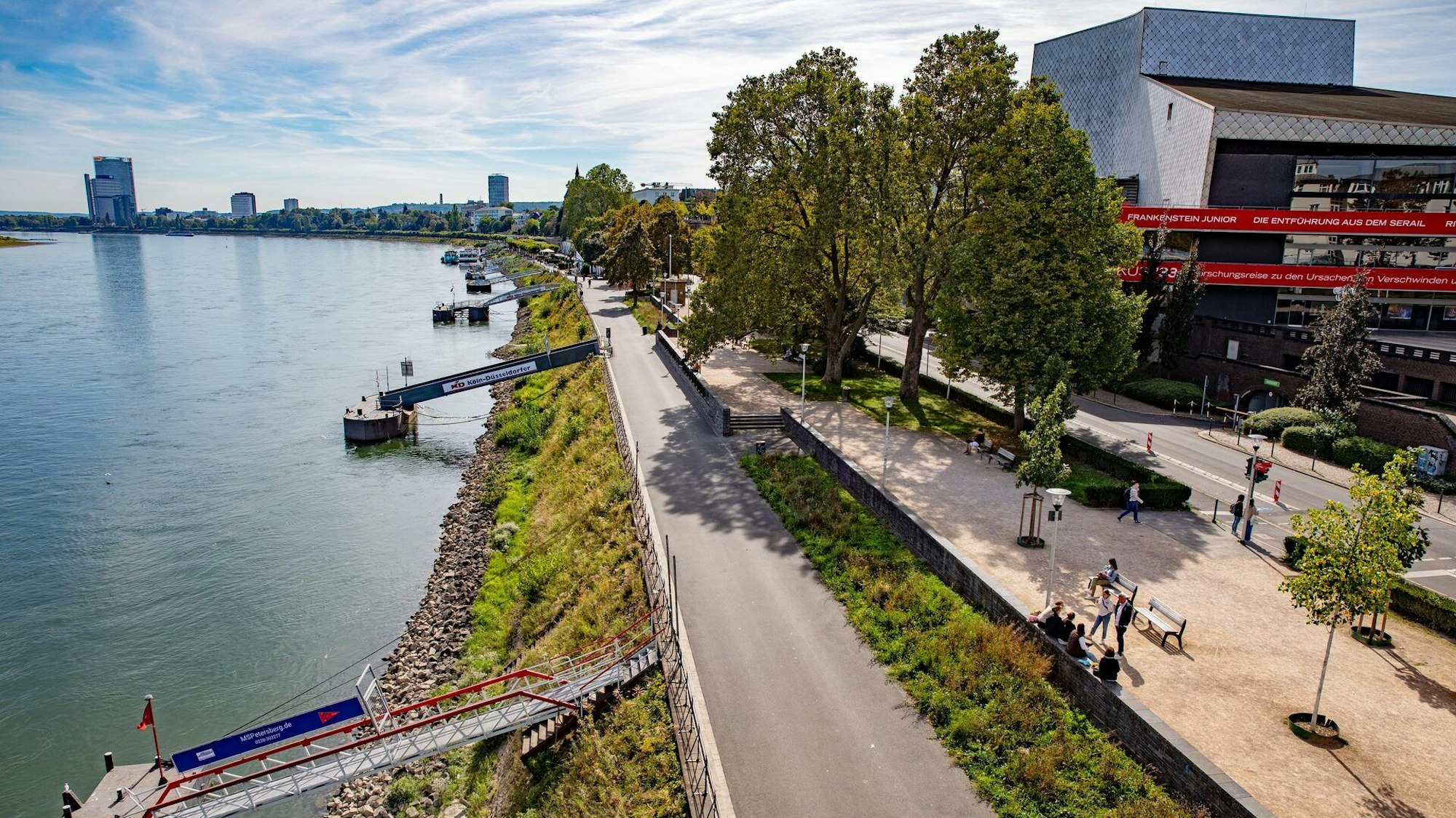Das Bonner Rheinufer mit Fuß- und Radweg, den Anlegern für Schiffe und Fähren und einem Blick auf das Stadtpanorama.