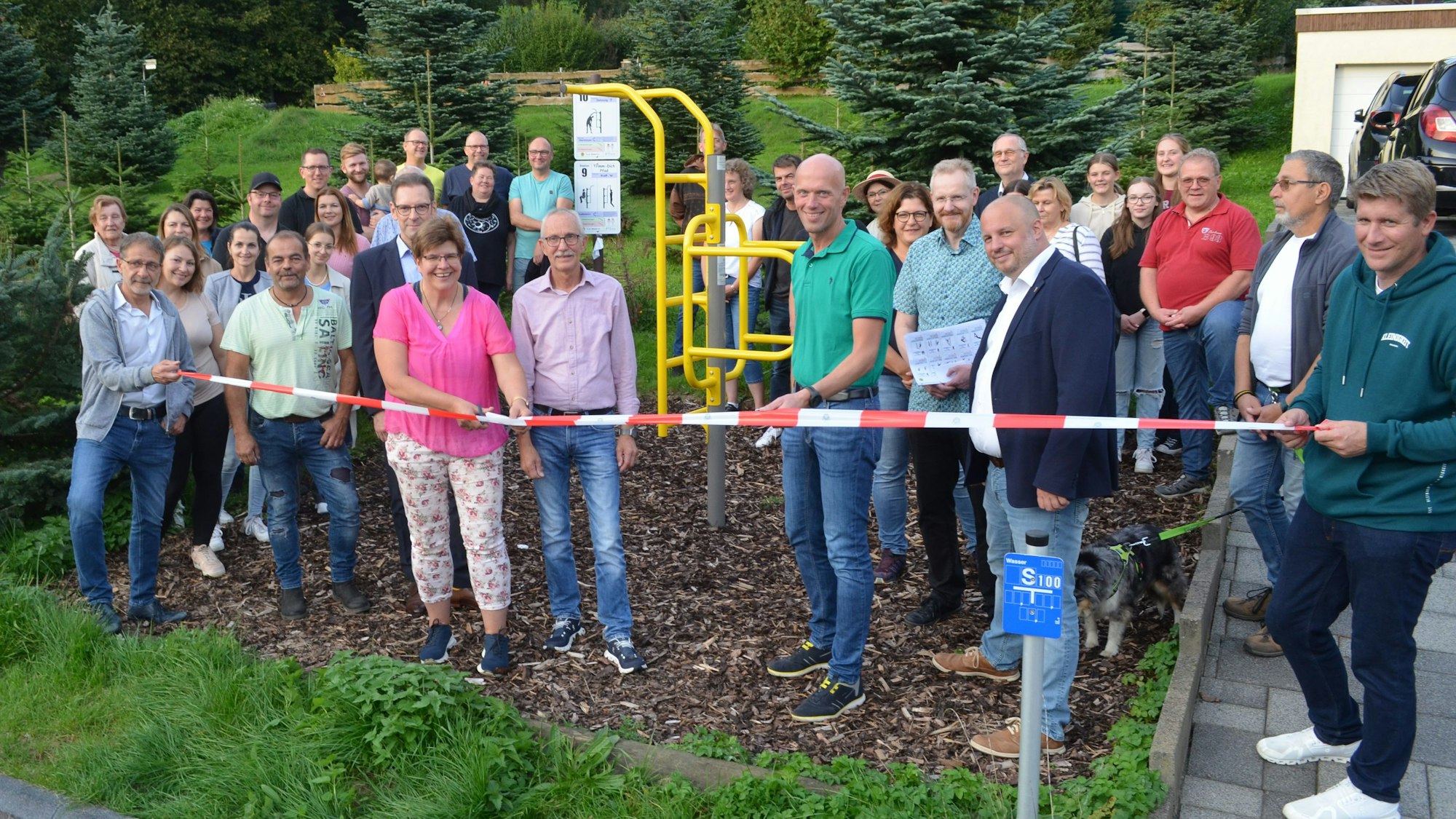 Zahlreiche Menschen stehen an einem neuen Fitnessparcours, der noch mit einem Flatterband abgesperrt ist. Eine Frau setzt eine Schere an das Band.