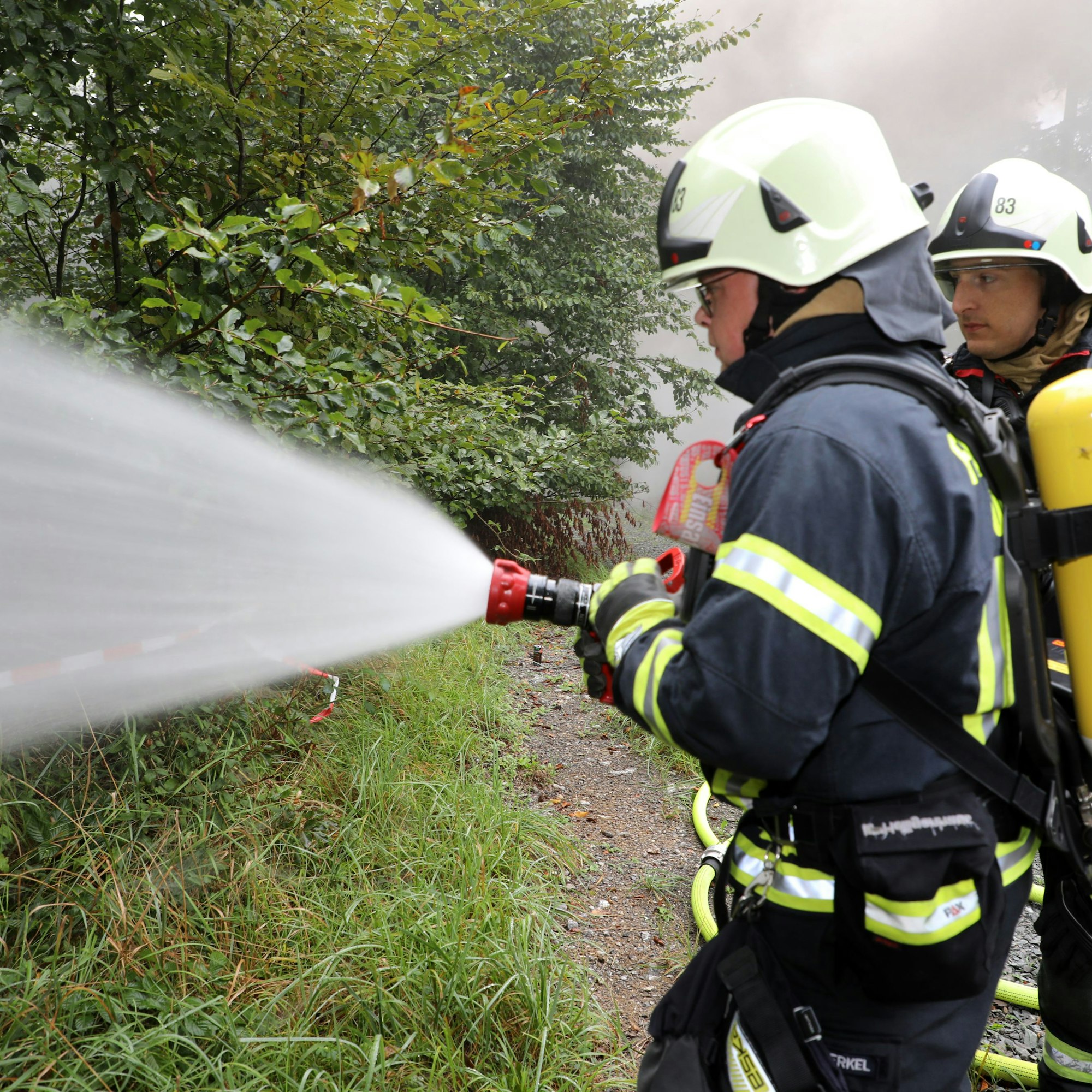 Ein Feuerwehrmann sprüht Wasser aus einem Feuerwehrschlauch in den Wald.