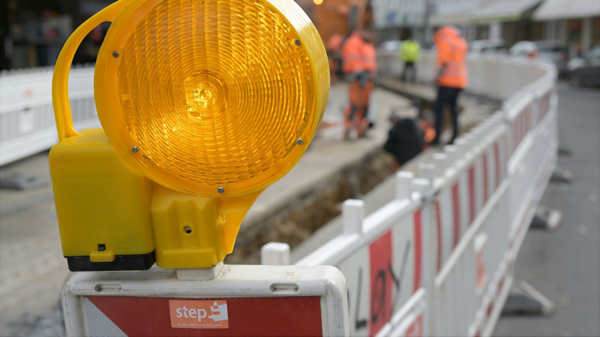 Im Vordergrund ist eine Bake mit gelber Warnbeleuchtung zu sehen. Dahinter stehen weitere rot-weiße Absperrungen.
