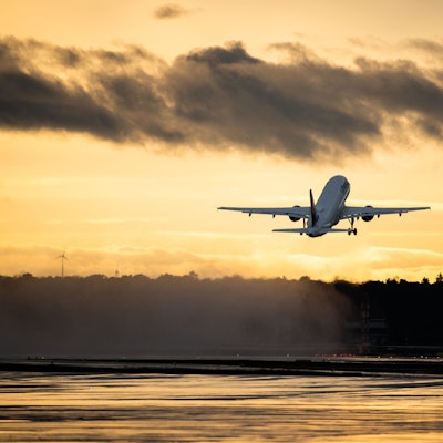 Ein startendes Flugzeug vor einem orangen Abendhimmel.