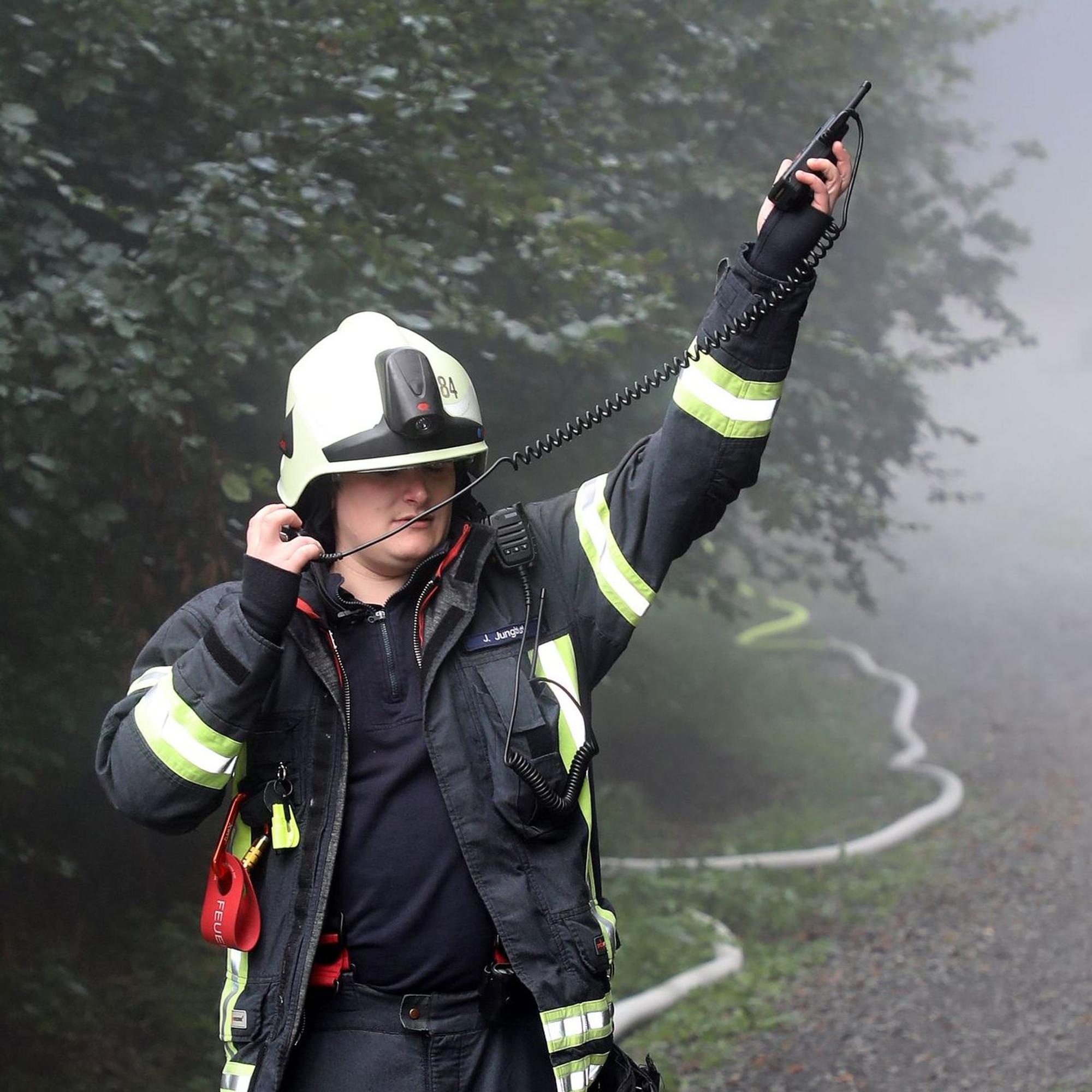 Ein Feuerwehrmann hält ein Funkgerät in die Luft und das Mikrofon mit Lautsprecher an sein Ohr.
