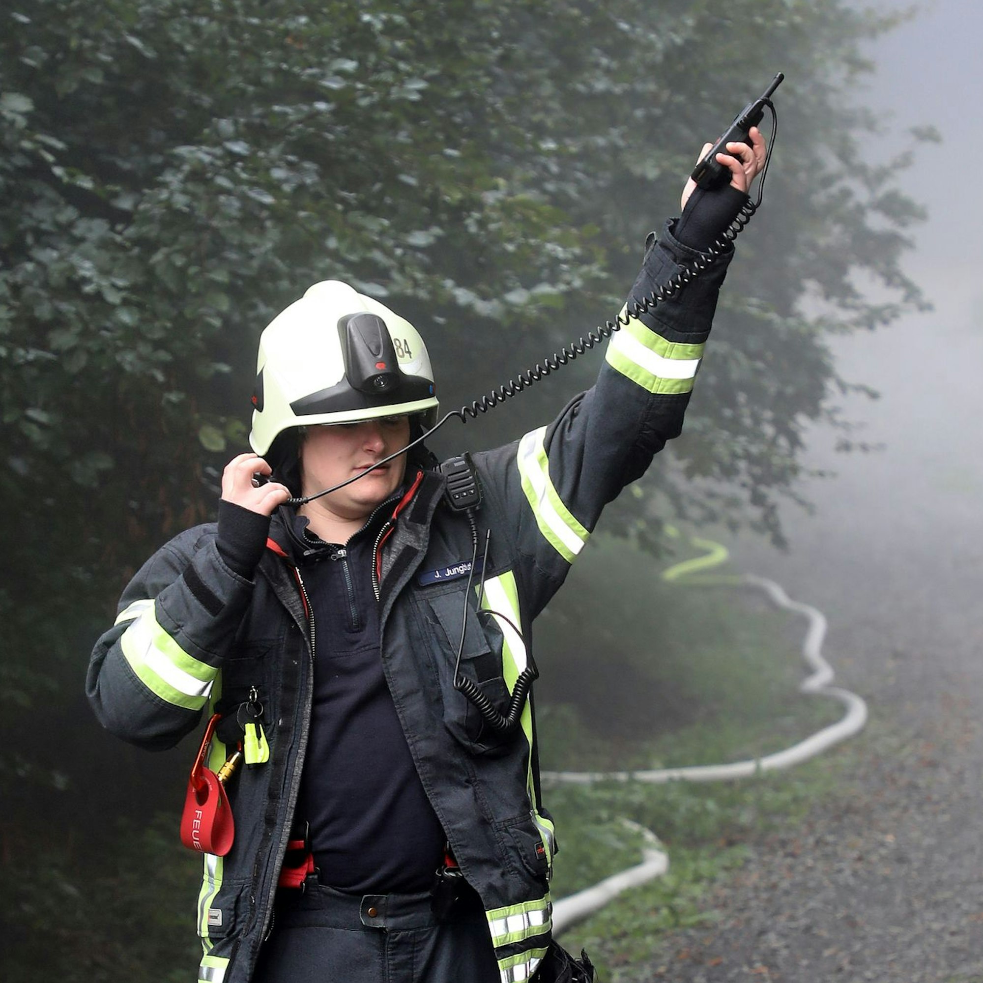 Ein Feuerwehrmann hält ein Funkgerät in die Luft und das Mikrofon mit Lautsprecher an sein Ohr.