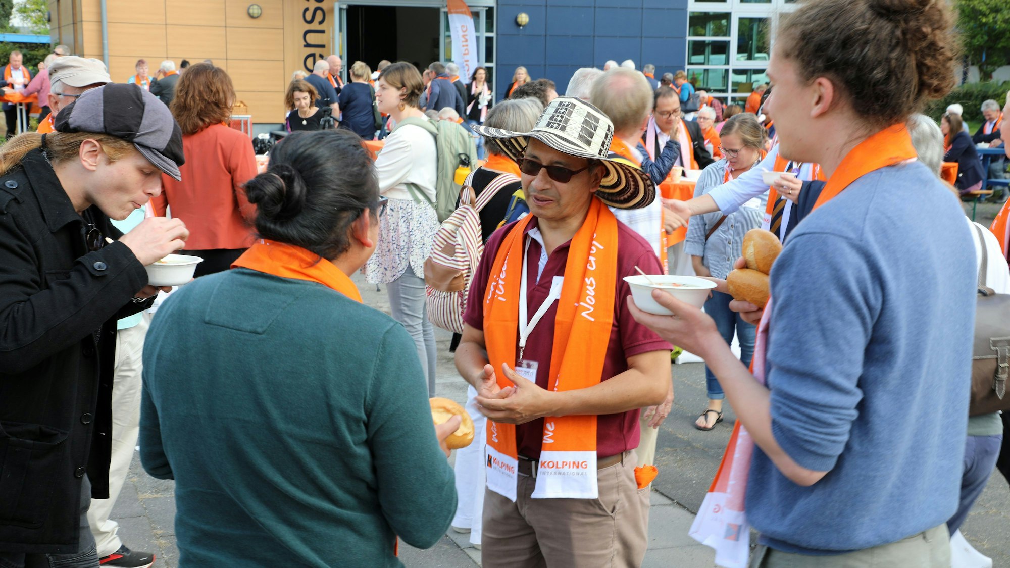 Menschen unterschiedlicher Hautfarbe stehen mit Suppenschüsseln in den Händen auf dem Schulhof des Albertus-Magnus-Gymnasiums in Bensberg zusammen.
