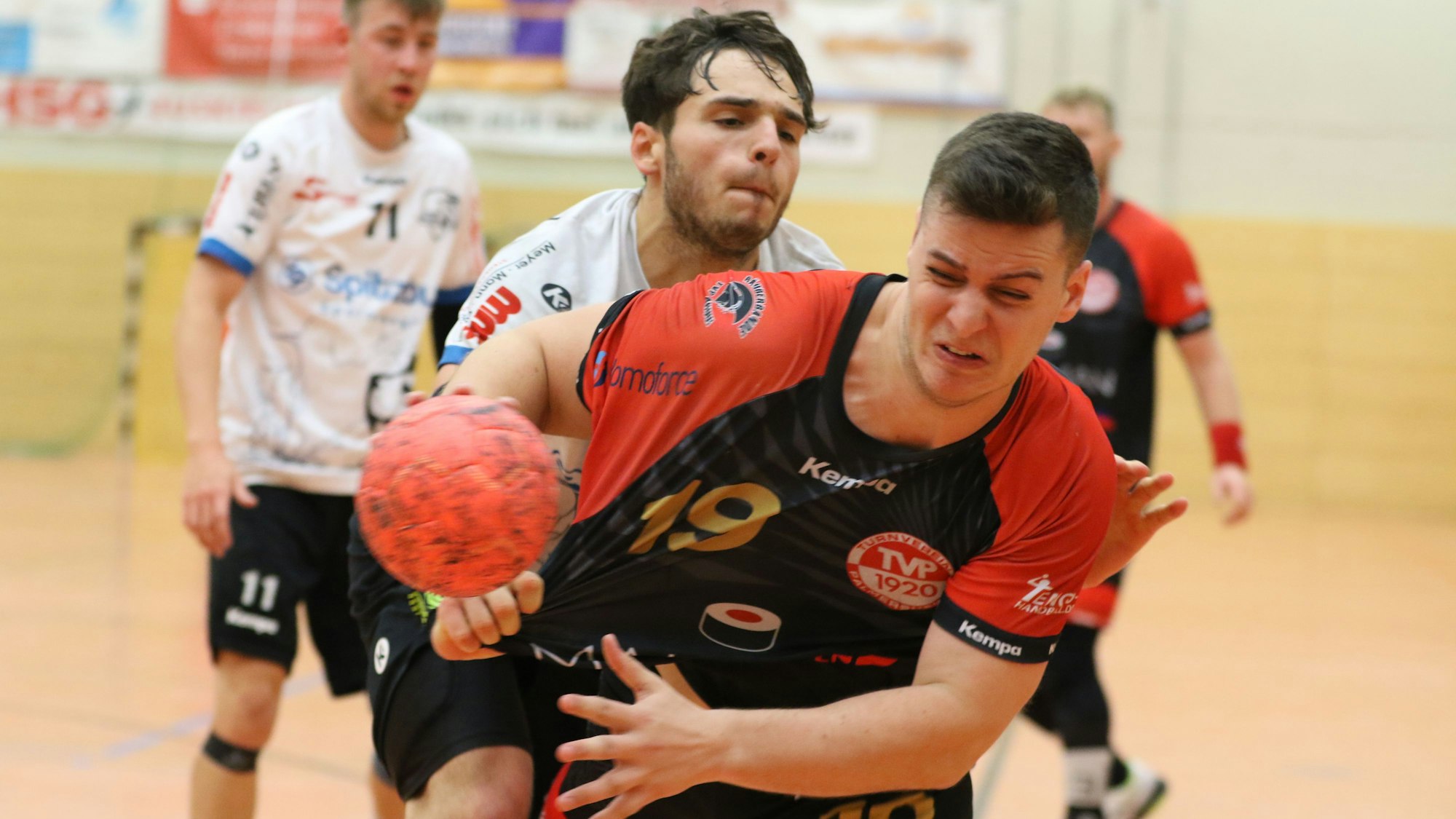 Ein Handballer mit einem Ball in der Hand wird vom Gegenspieler attackiert und am Trikot gezogen.