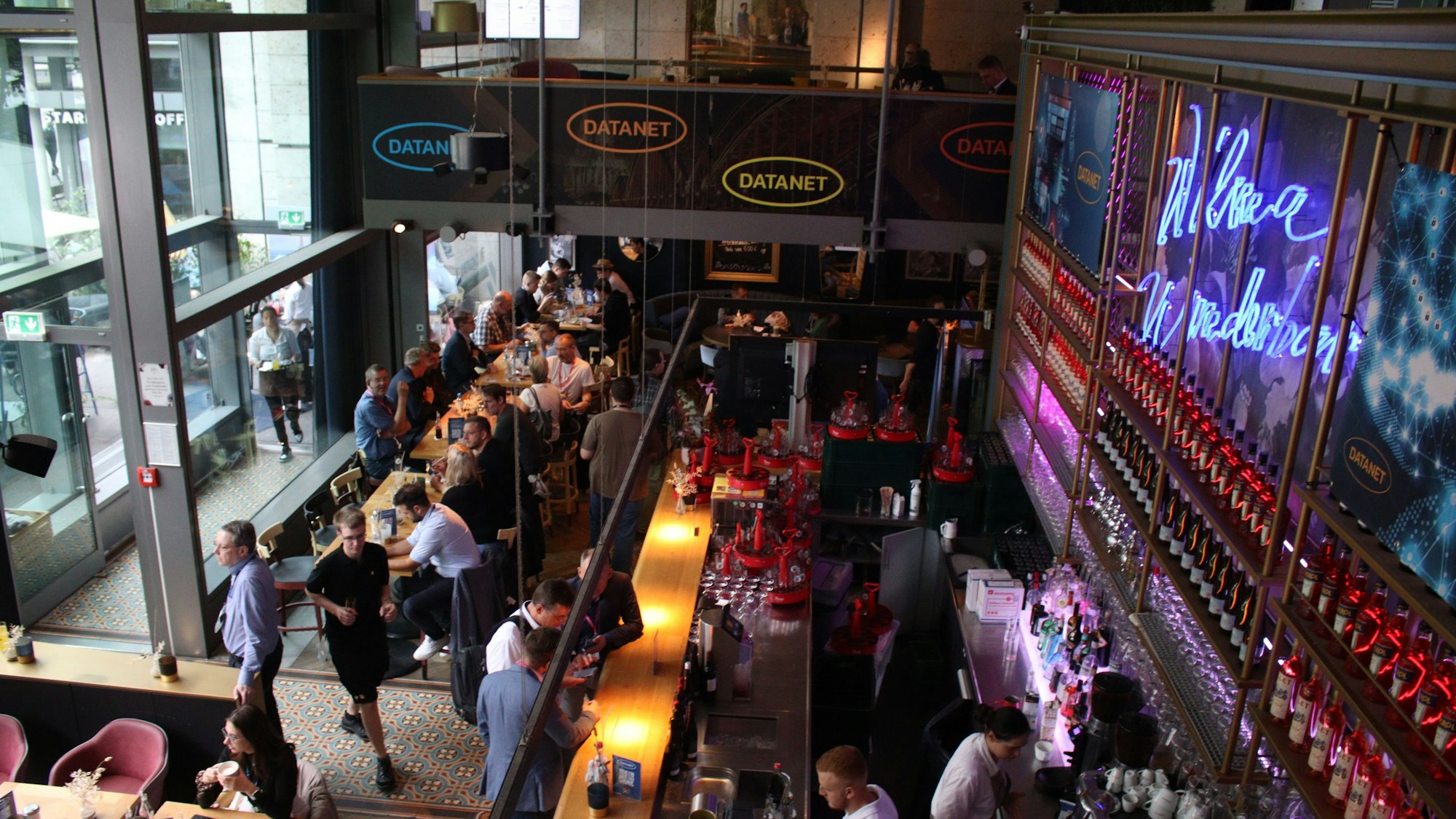 Menschen unterhalten sich in Kneipenstimmung. Das Datanet-Logo prangt an den Wänden.