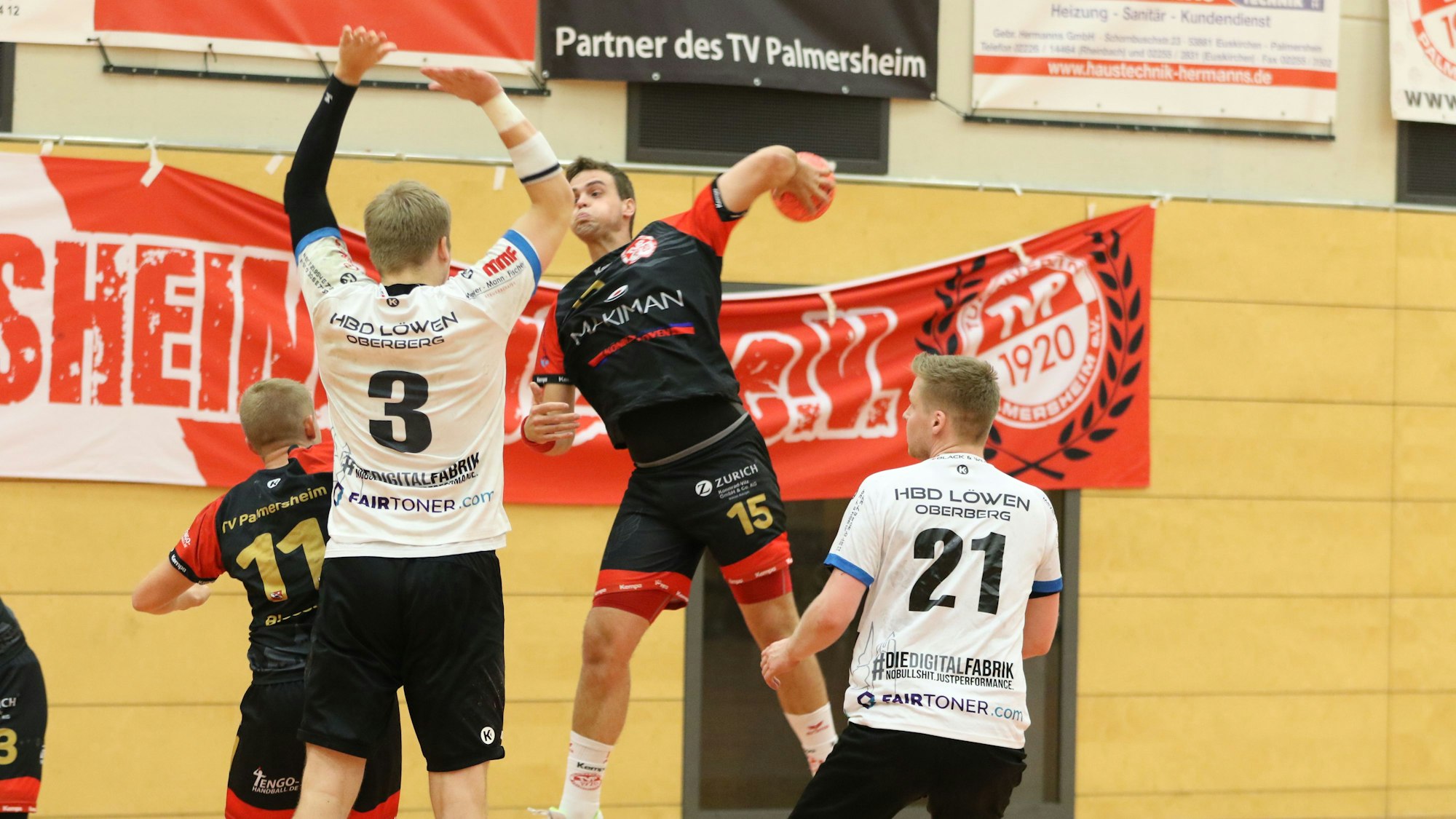 Ein Palmersheimer Handballer setzt zum Sprungwurf an, der Arm, in dessen Hand der Ball ist, ist weit ausgeholt. Ein Gegenspieler springt mit gehobenen Armen hoch.