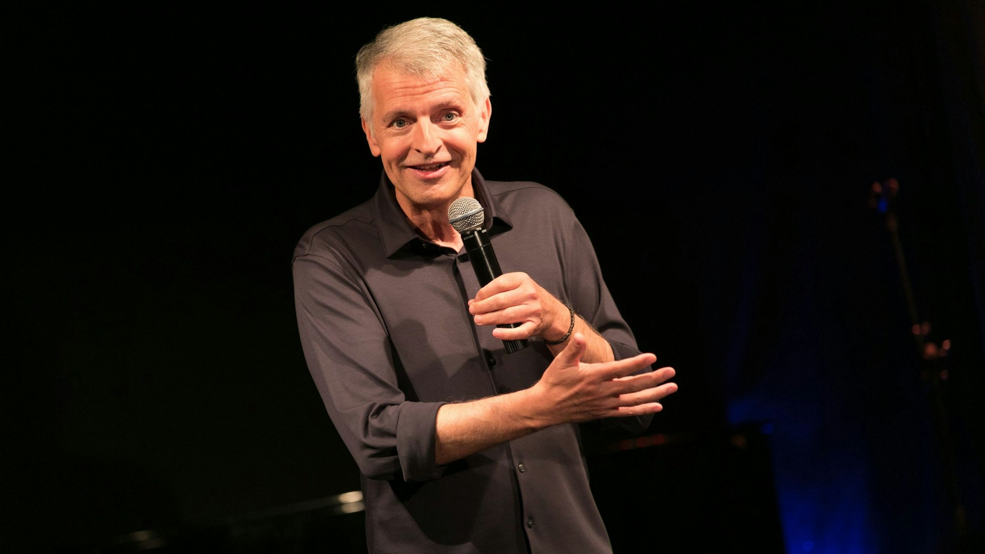 Johannes Flöck gestikuliert mit einem Mikrofon in der Hand.