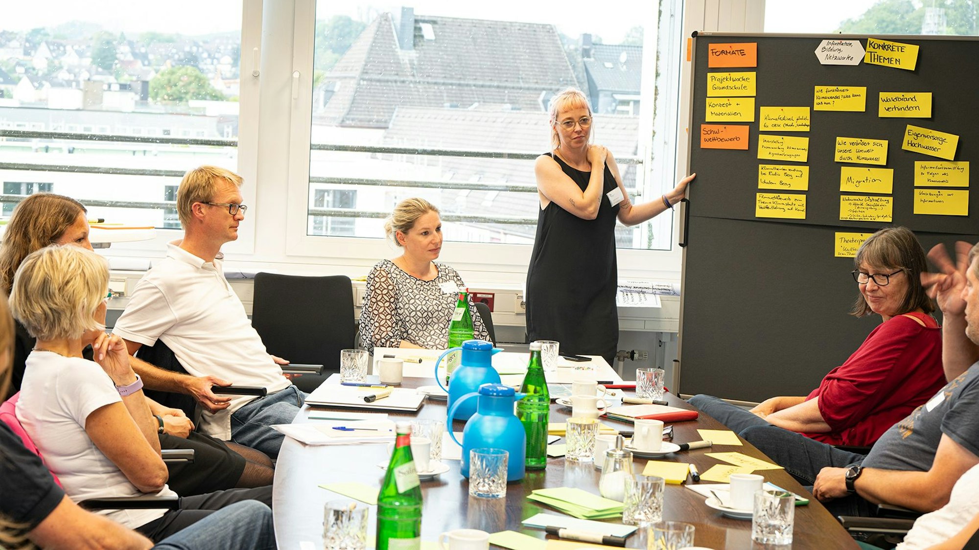Eine Gruppe sitzt bei einem Workshop zusammen und schaut gemeinsam auf Notizen an einer Flipchart.