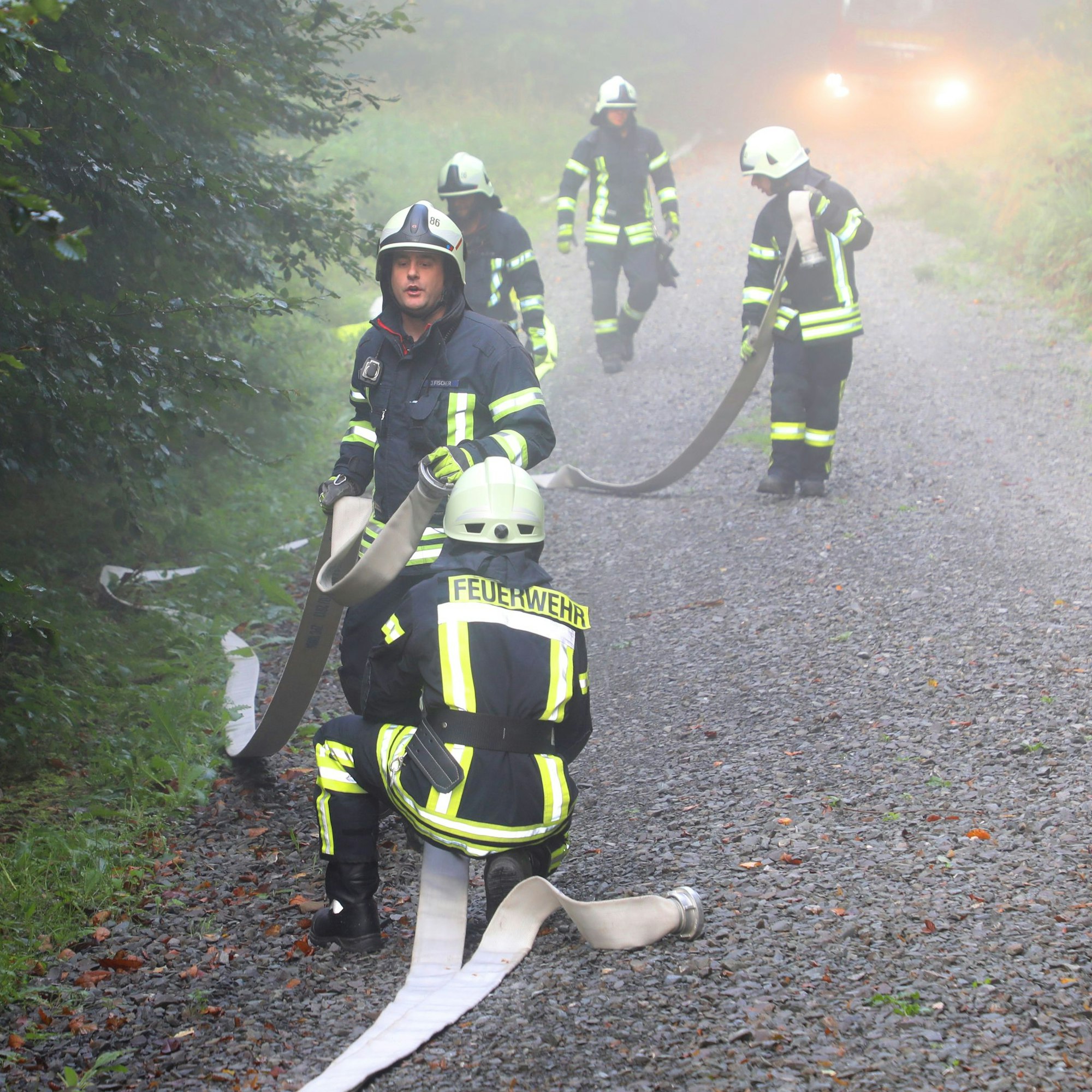 Feuerwehrleute rollen Schläuche aus und verlegen sie entlang eines Waldwegs.