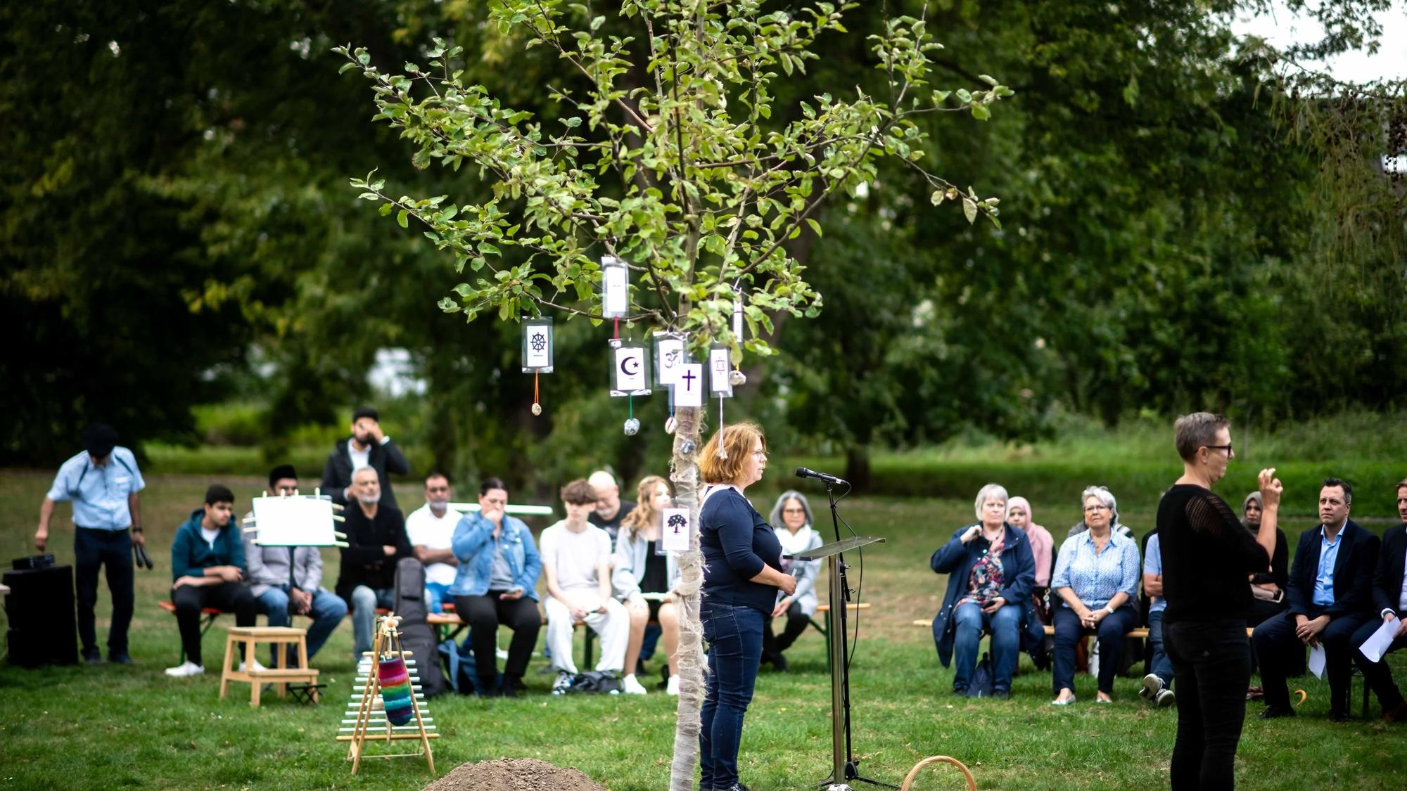 Das Bild zeigt den Apfelbaum im Vordergrund. Im Hintergrund sind zahlreiche Gäste zu sehen.