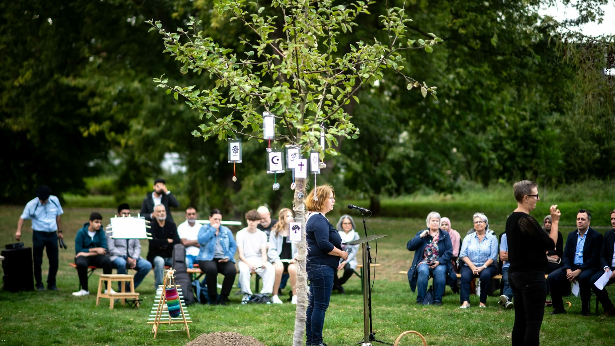 Das Bild zeigt den Apfelbaum im Vordergrund. Im Hintergrund sind zahlreiche Gäste zu sehen.
