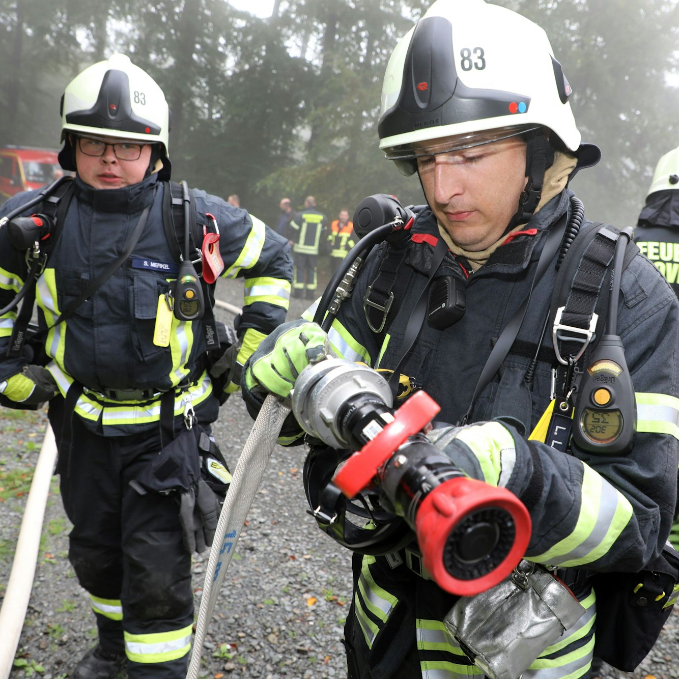 Zwei Feuerwehrleute montieren eine Düse an einen Feuerwehrschlauch.