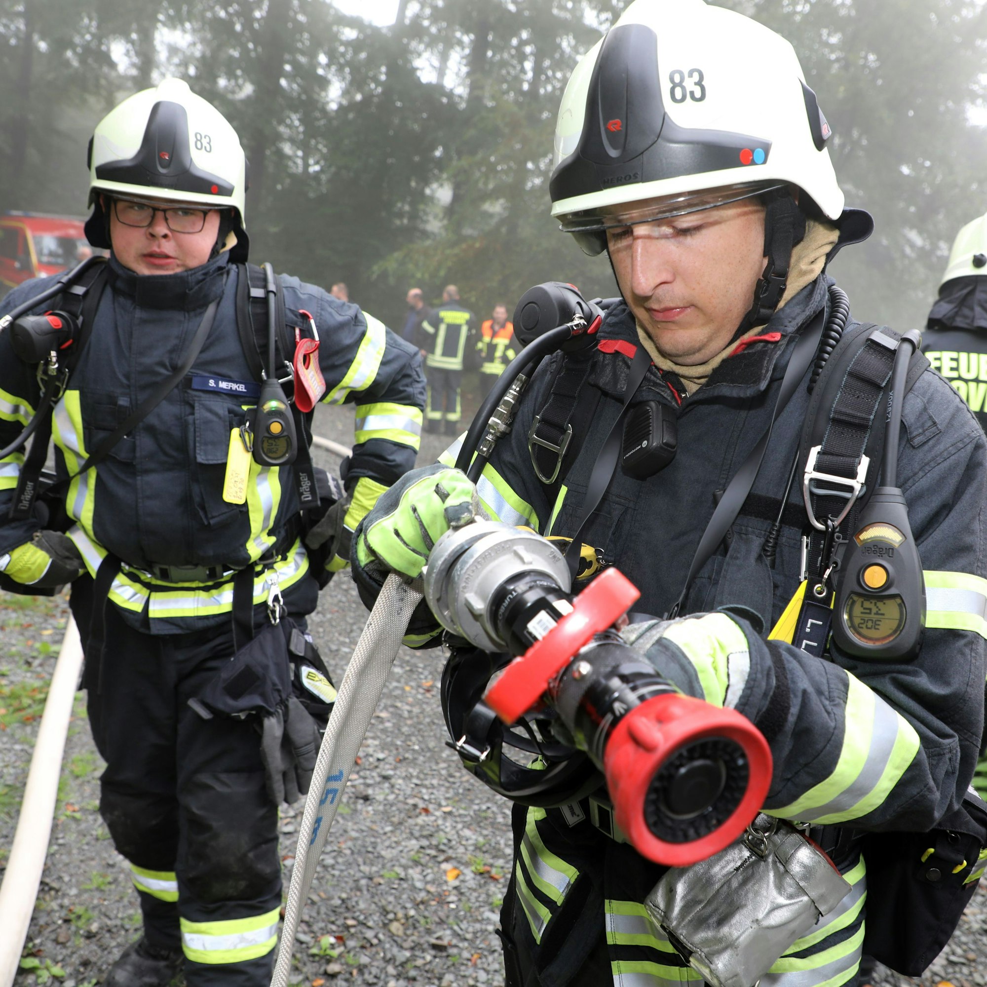 Zwei Feuerwehrleute montieren eine Düse an einen Feuerwehrschlauch.
