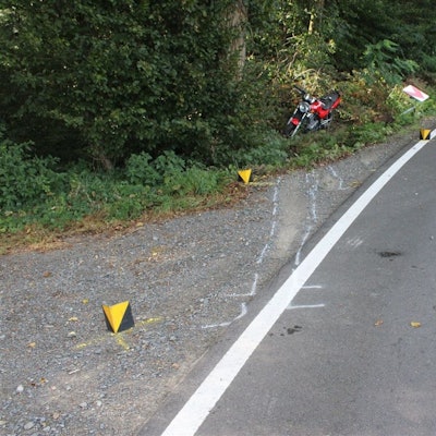 Ein Motorrad steht nach einem Unfall im Straßengraben, Markierungen der Polizei sind auf der Straße zu sehen und ein herausgerissenes Verkehrsschild.