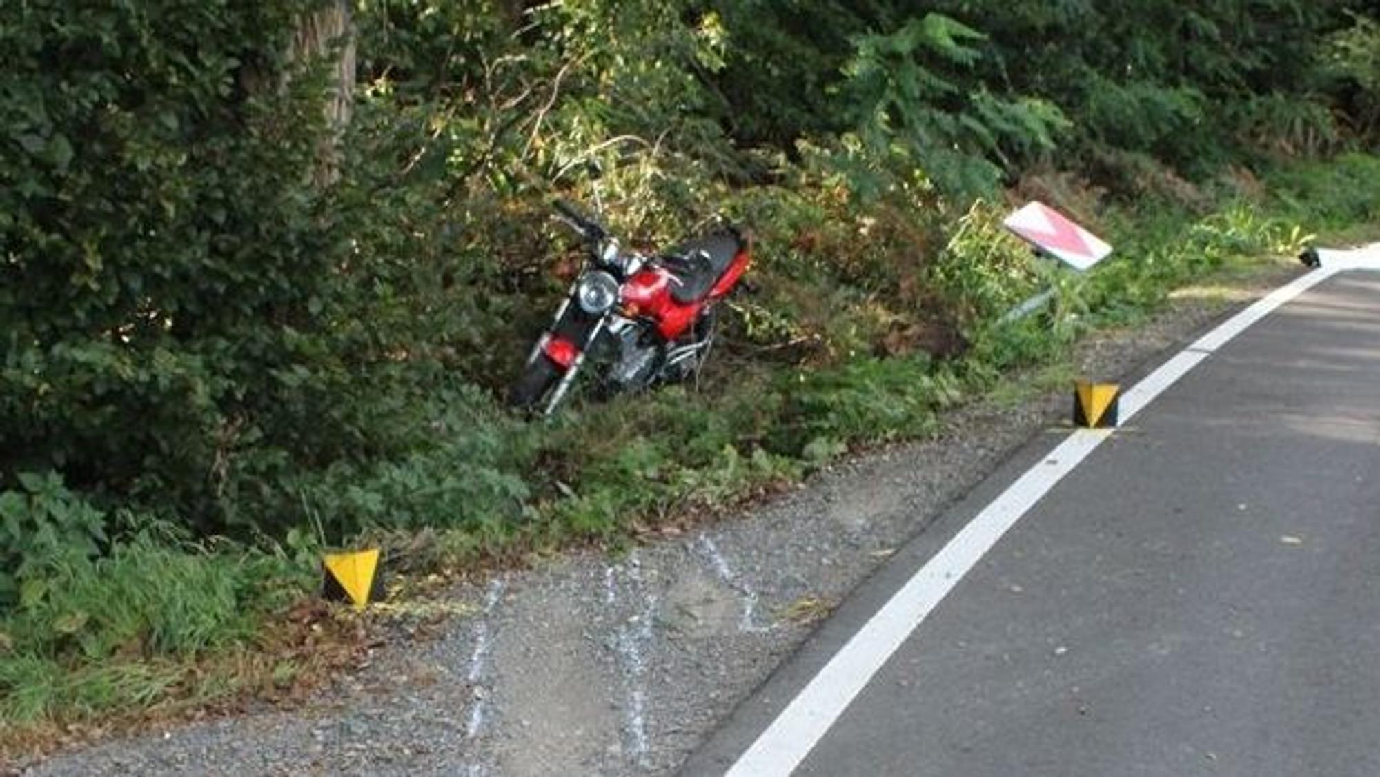 Ein Motorrad steht nach einem Unfall im Straßengraben, Markierungen der Polizei sind auf der Straße zu sehen und ein herausgerissenes Verkehrsschild.