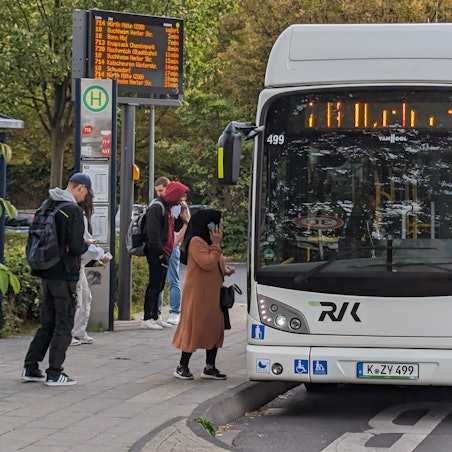 Ein Stadtbus an einer Bushaltestelle mit wartenden Menschen.