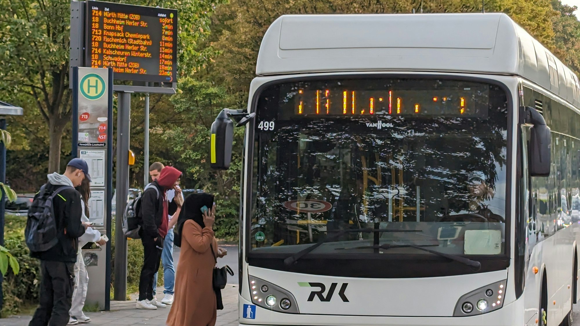 Ein Stadtbus an einer Bushaltestelle mit wartenden Menschen.