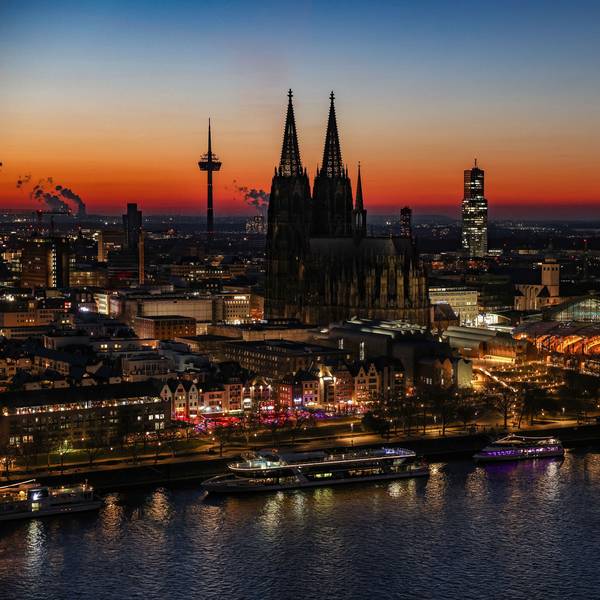 Der Himmel färbt sich hinter dem Rheinpanorama mit Dom und Hauptbahnhof nach Sonnenuntergang rötlich.