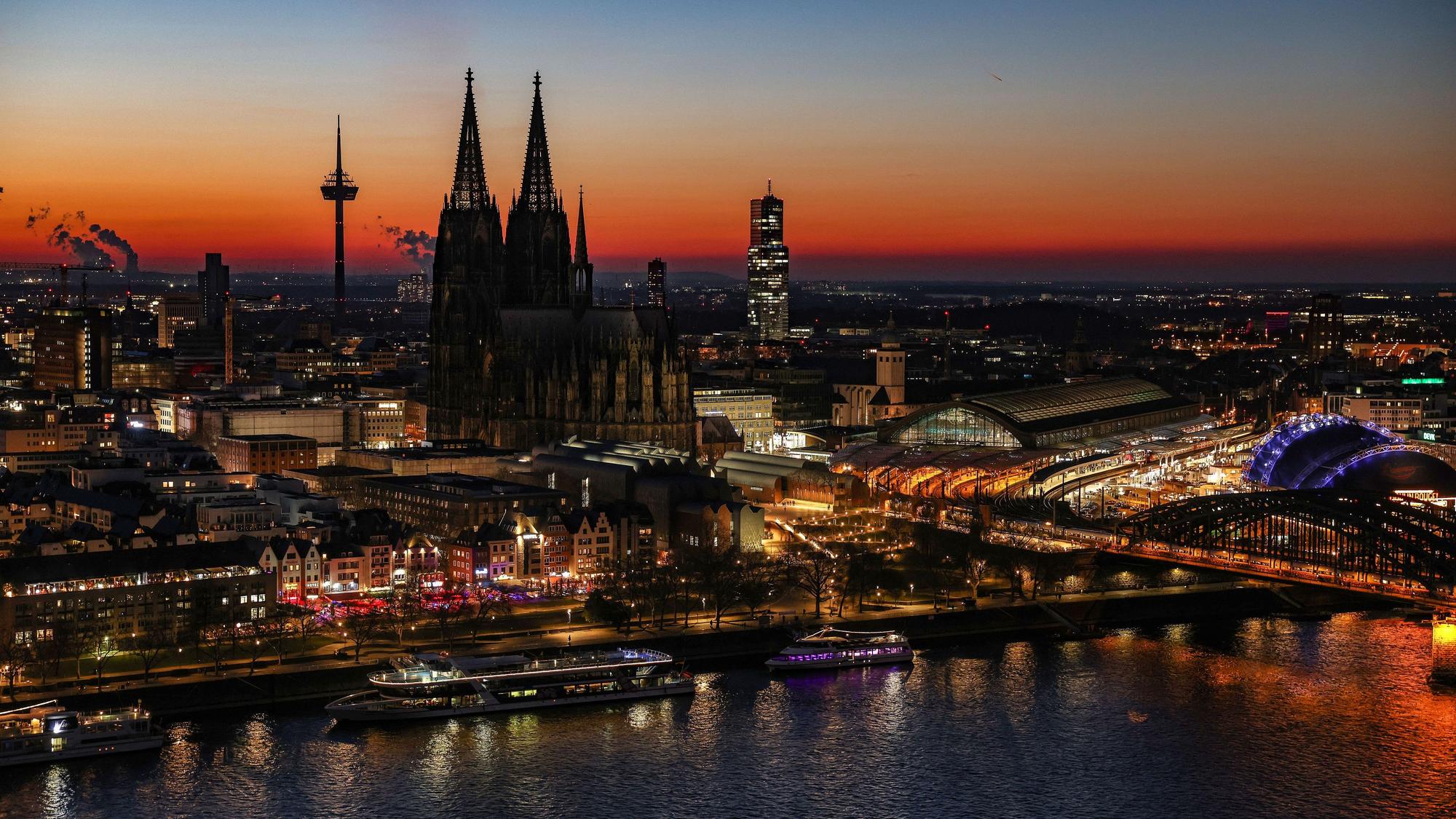 Der Himmel färbt sich hinter dem Rheinpanorama mit Dom und Hauptbahnhof nach Sonnenuntergang rötlich.