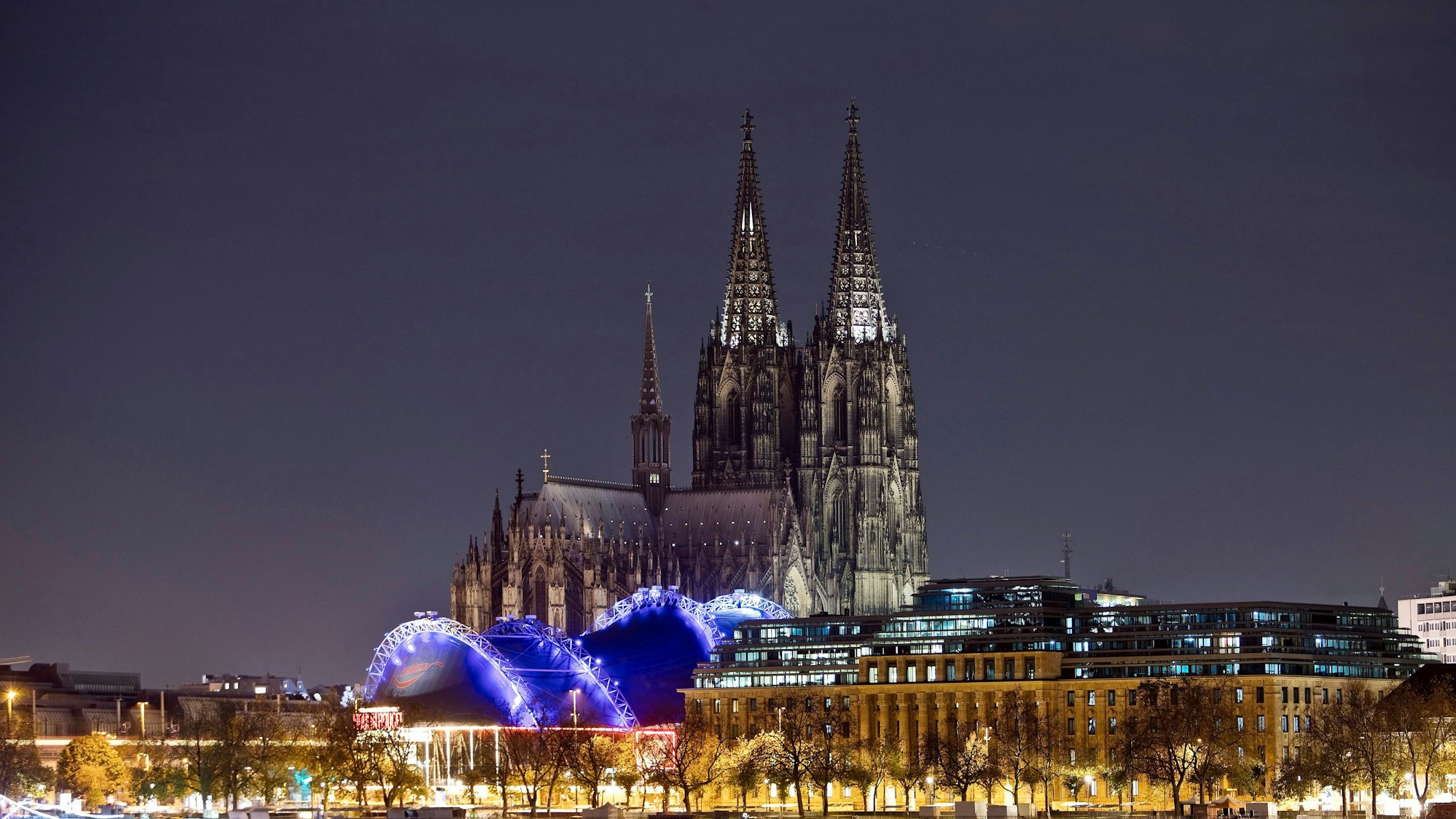 Das Kölner Stadtpanorama mit nur schwach beleuchtetem Koelner Dom, Musical Dome und dem Rhein in der Nacht (Symbolbild)