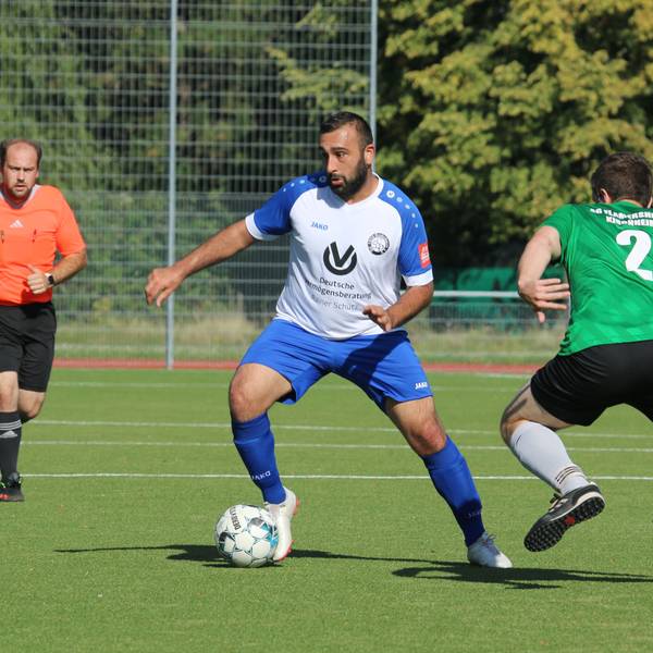 Ein Fußballer führt den Ball, ein Gegner hat ihn im Visier. Der Schiedsrichter beobachtet die Szene.