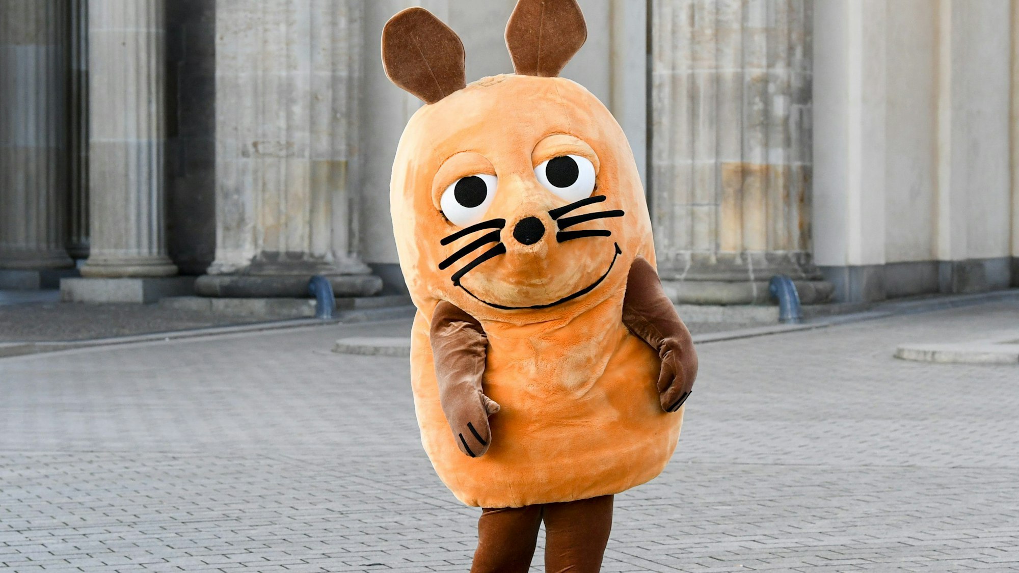 Eine „Maus“-Figur steht vor dem Brandenburger Tor.
